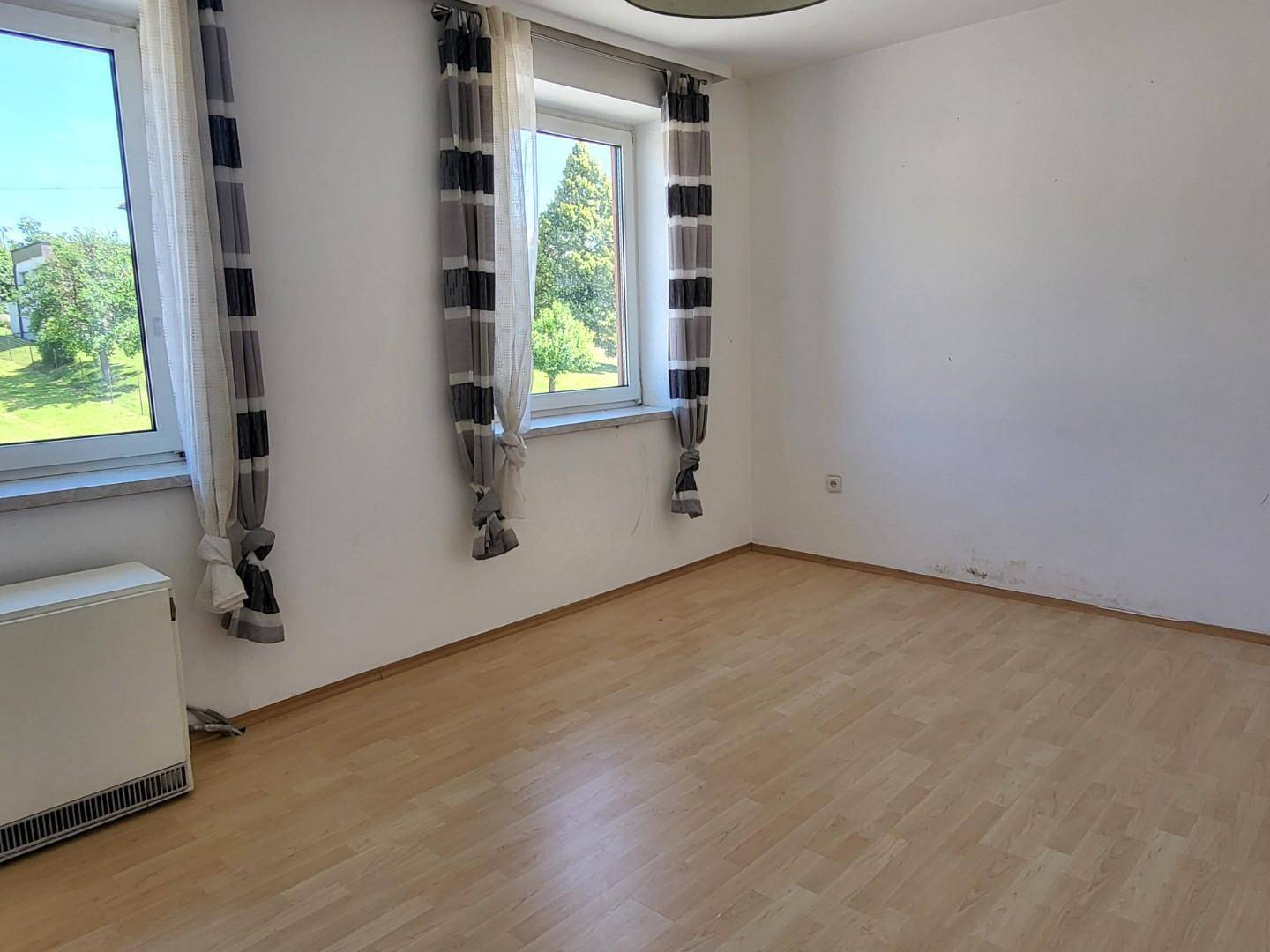 Helles Schlafzimmer mit Laminatboden, zwei Fenstern und Blick ins Grüne.