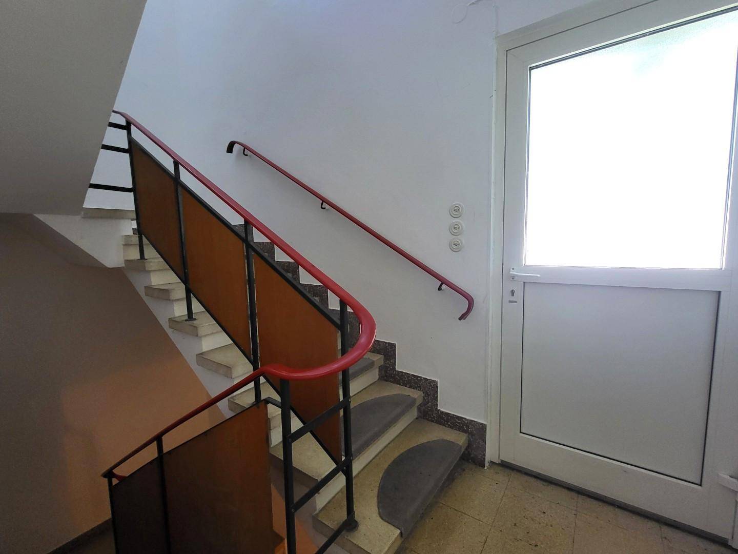Treppenhaus mit roten Handläufen und Zugangstür, das verschiedene Etagen verbindet.