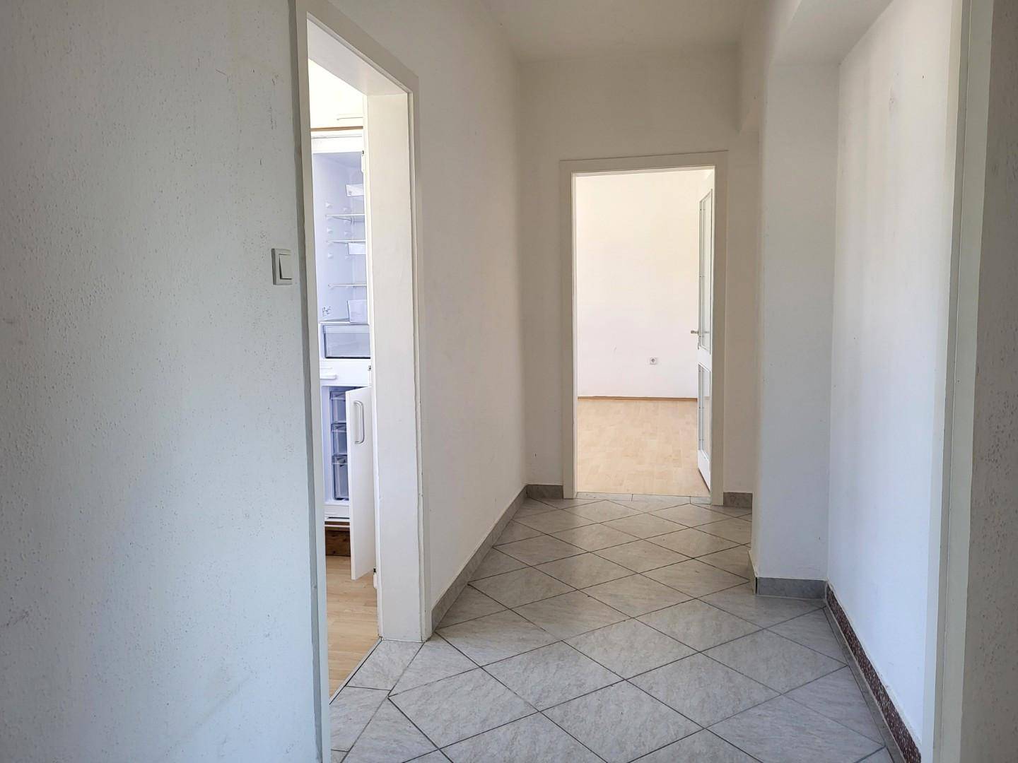 Heller Flur mit Fliesenboden und Zugang zu weiteren Räumen, inklusive Blick auf einen Kühlschrank.