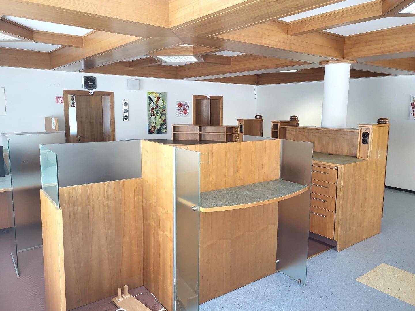Großraumbüro mit Holzdeckenbalken und mehreren Arbeitsplätzen, teilweise mit Glasabtrennungen.