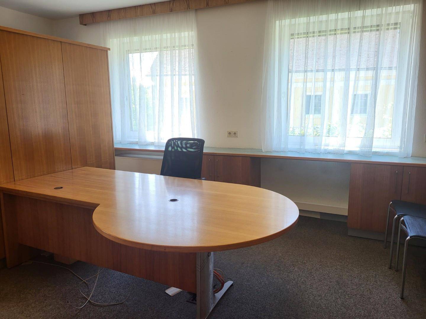 Helles Büro mit Holzschreibtisch, Schrank und zwei Fenstern, ideal für konzentriertes Arbeiten.