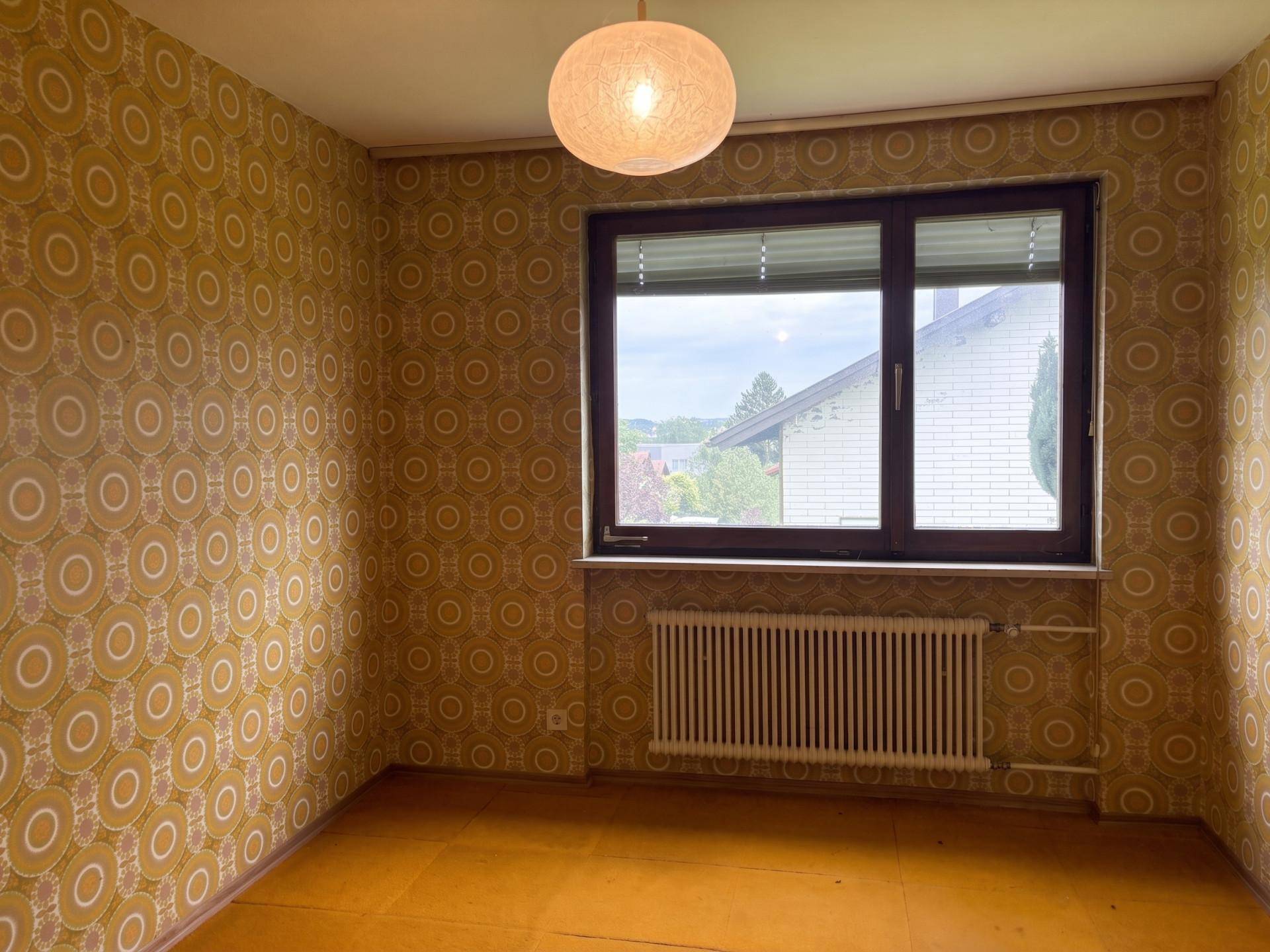 Zimmer mit auffälliger gemusterter Tapete und großem Fenster, das viel Tageslicht in den Raum lässt.