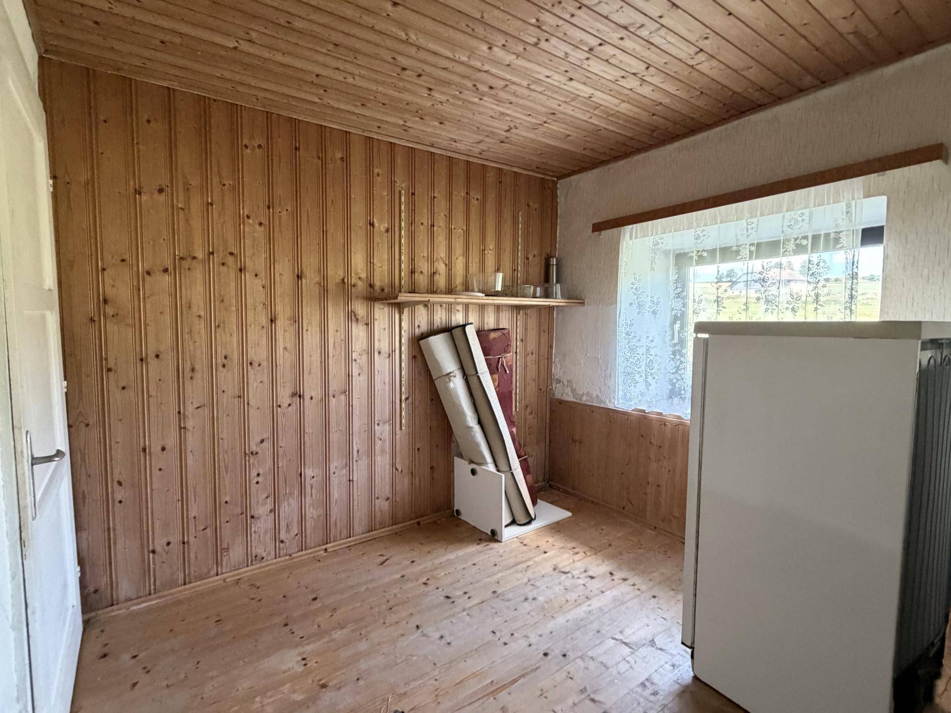 Einfaches Zimmer mit Holzvertäfelung an Wänden und Decke, mit Blick ins Grüne.