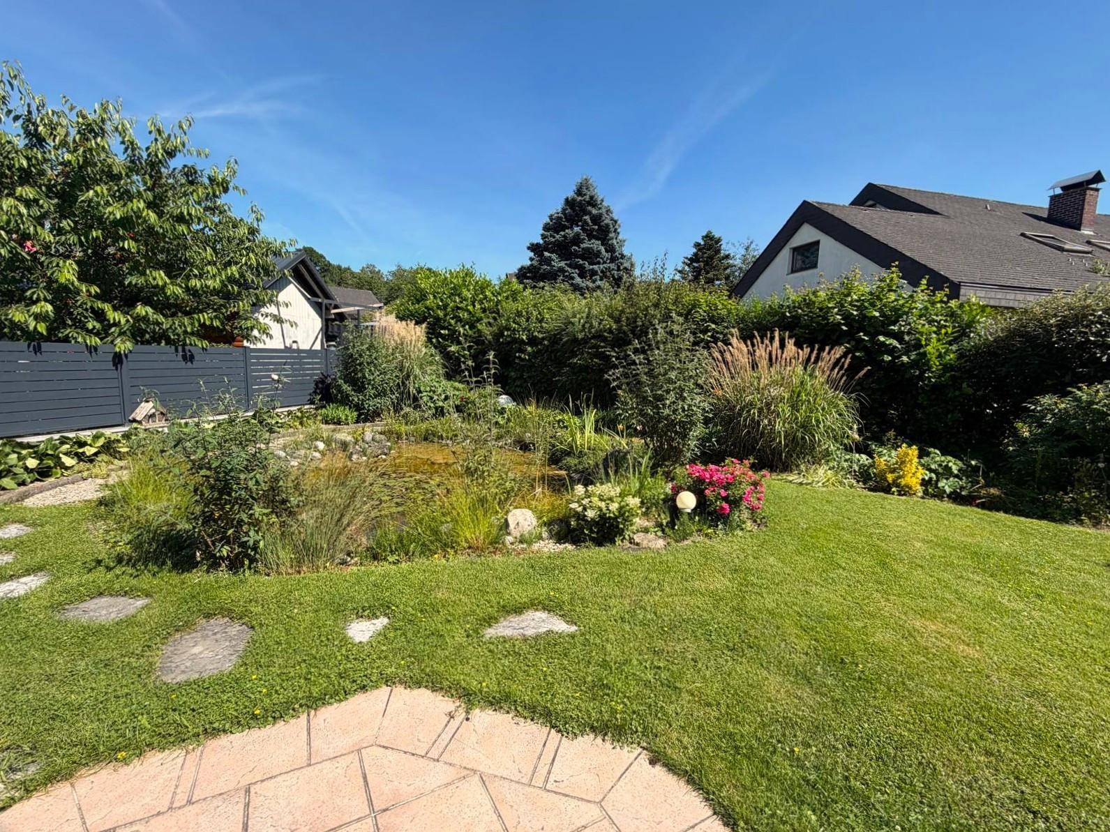 Gartenbereich mit einem kleinen Teich, umgeben von üppiger Vegetation und Rasen.