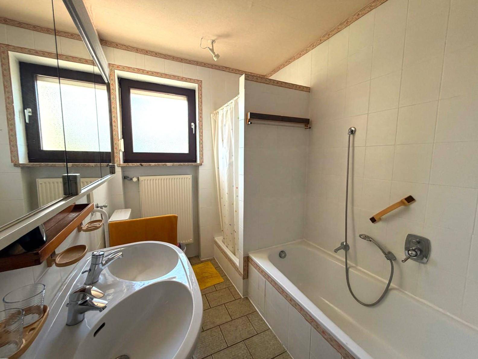 Badezimmer mit Doppelwaschbecken, Badewanne mit Duschvorhang und zwei Fenstern.