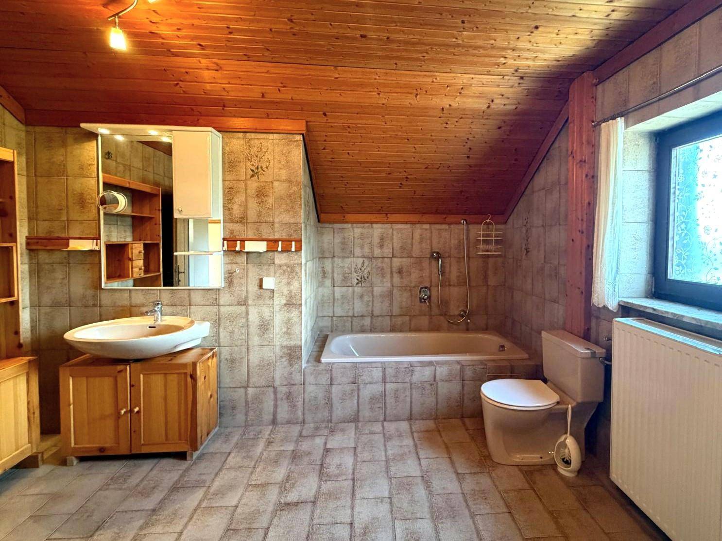 Badezimmer im Dachgeschoss mit Holzdecke, gefliesten Wänden und Badewanne.