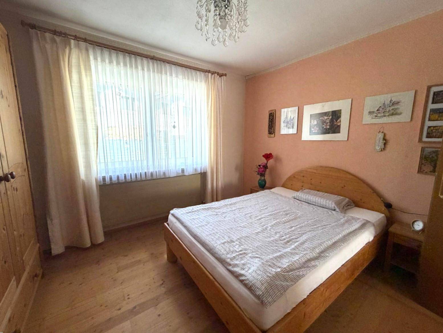 Schlafzimmer mit Holzbett, pfirsichfarbenen Wänden und großem Fenster mit Vorhängen.