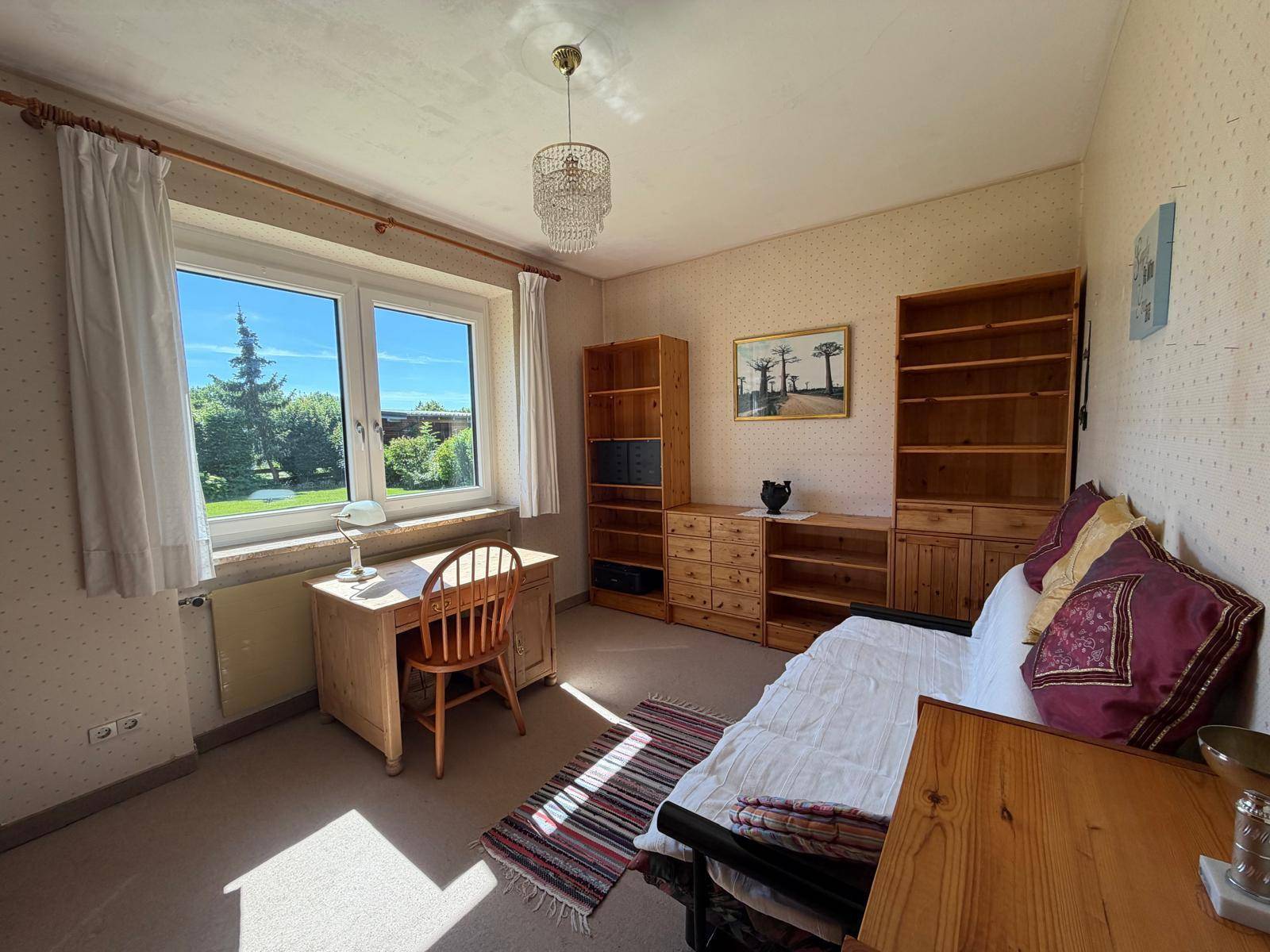 Arbeitszimmer mit Schreibtisch, Holzregalen und einem Fenster mit Blick in den Garten.