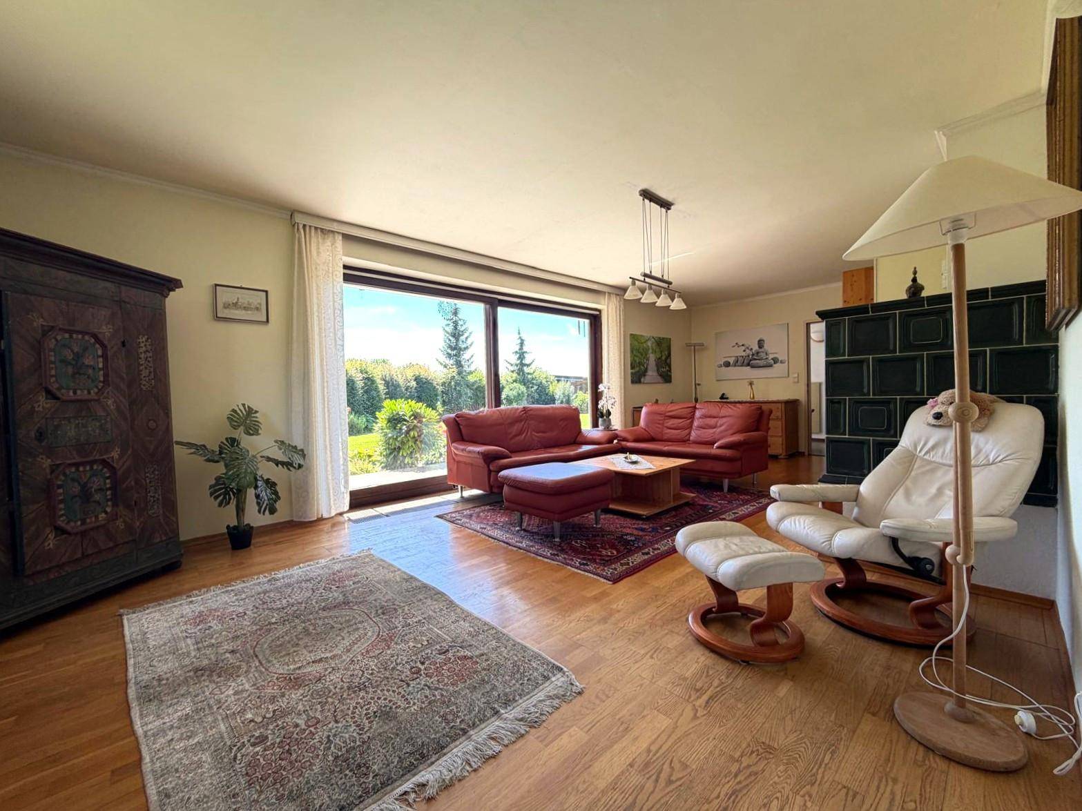 Helles Wohnzimmer mit roten Sofas, Holzboden, großem Fenster und traditionellem Kachelofen.