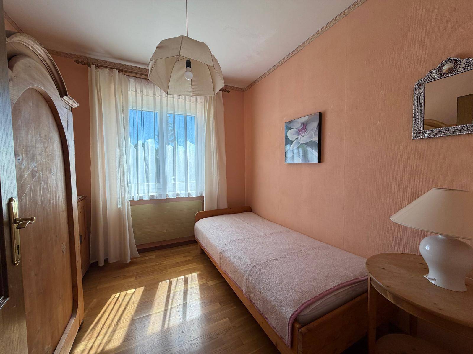 Kleines Schlafzimmer mit Einzelbett, pfirsichfarbenen Wänden und einem Fenster.