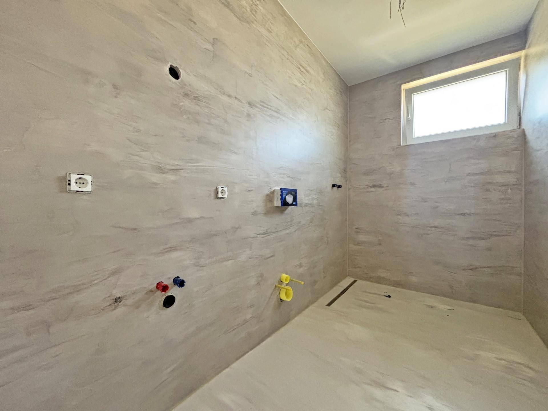 Unfertiges Badezimmer mit modernen Fliesen und vorbereiteten Anschlüssen für Sanitärobjekte.