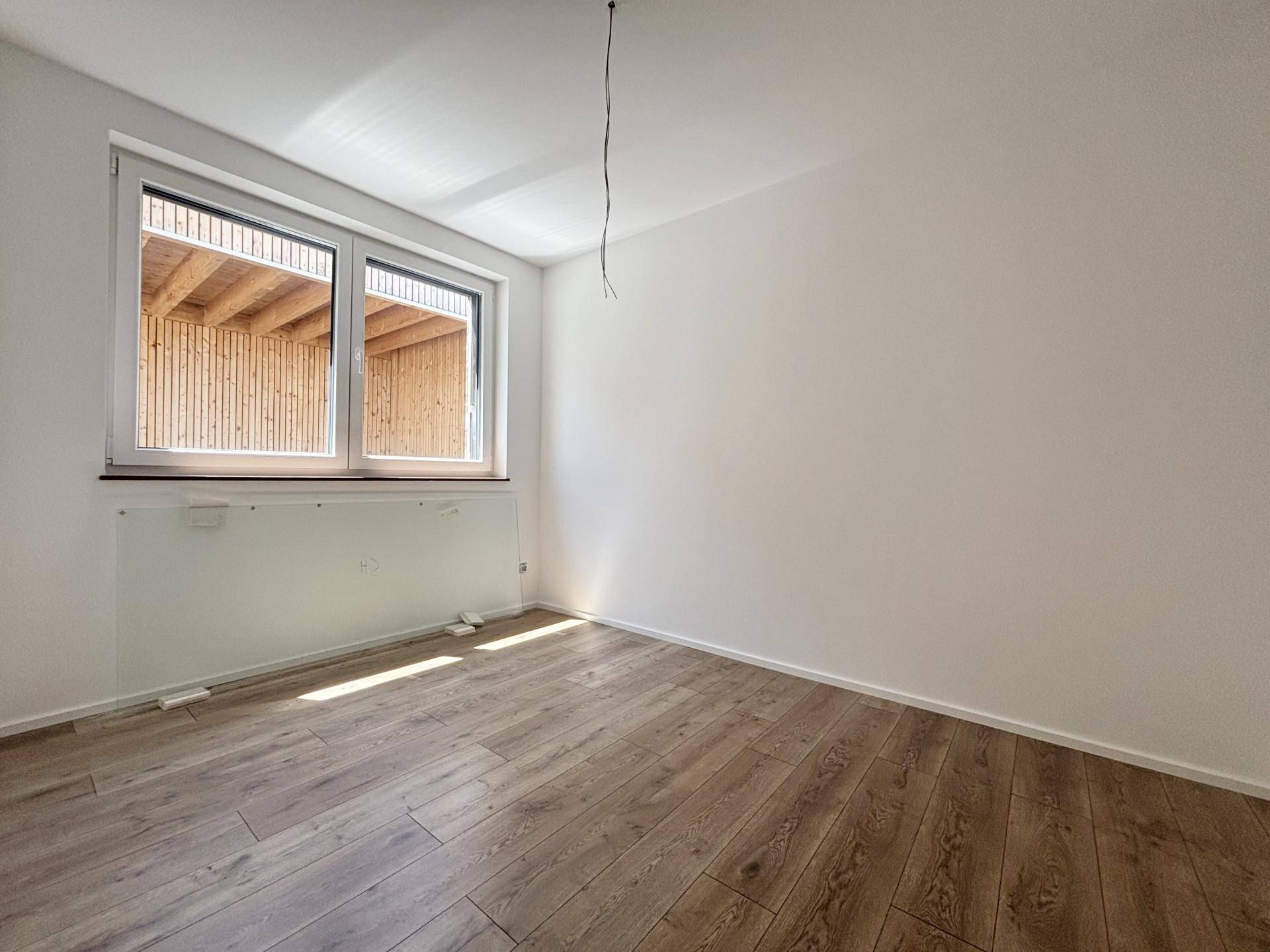 Helles Schlafzimmer mit Holzboden und großem Fenster, das viel Tageslicht hereinlässt.