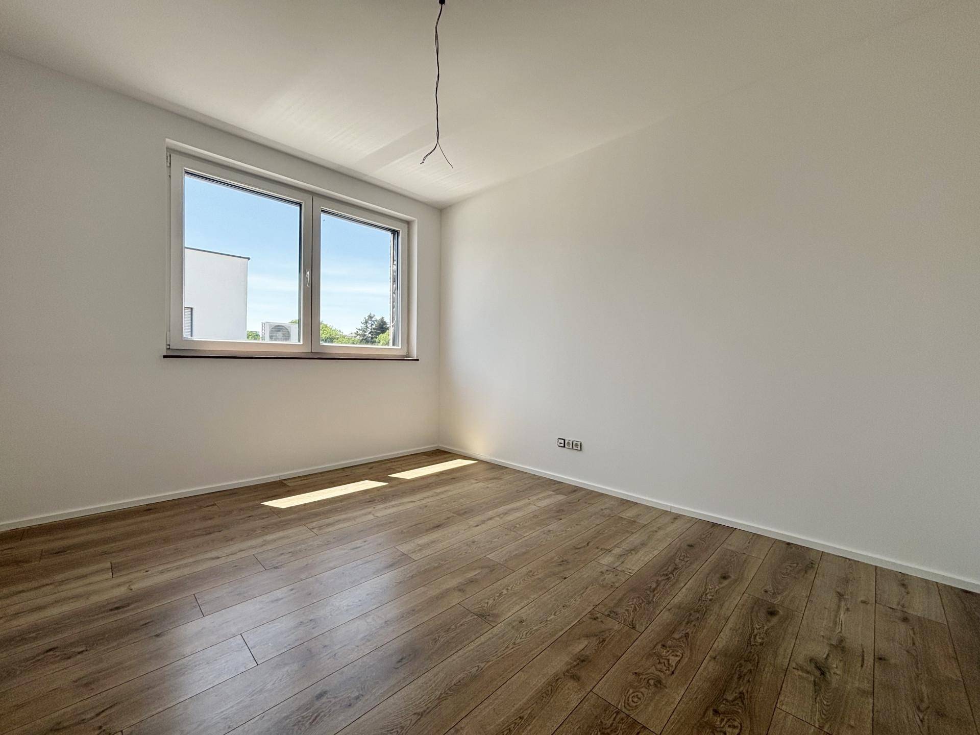 Helles Zimmer mit Holzboden und Fenster, das einen Blick ins Grüne ermöglicht.