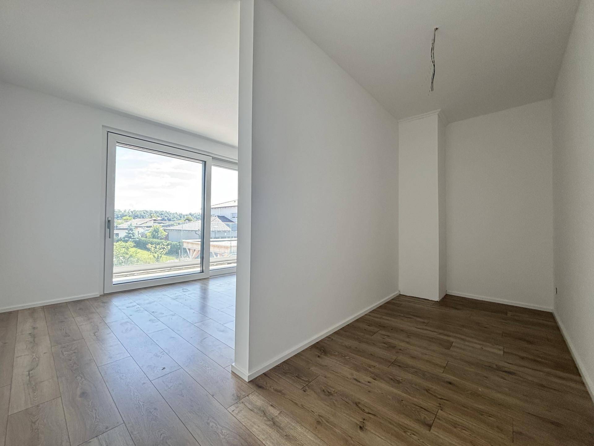 Helles Zimmer mit Holzboden und großem Fenster, das einen weiten Blick bietet.