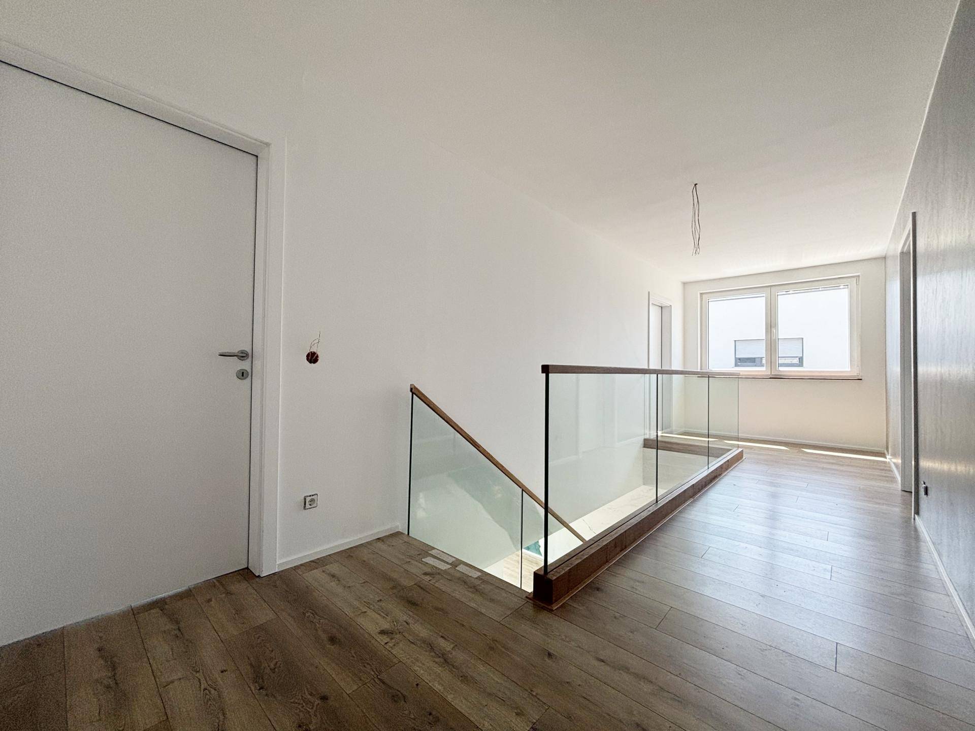 Heller Flur im Obergeschoss mit moderner Glasbrüstung und Holzboden.