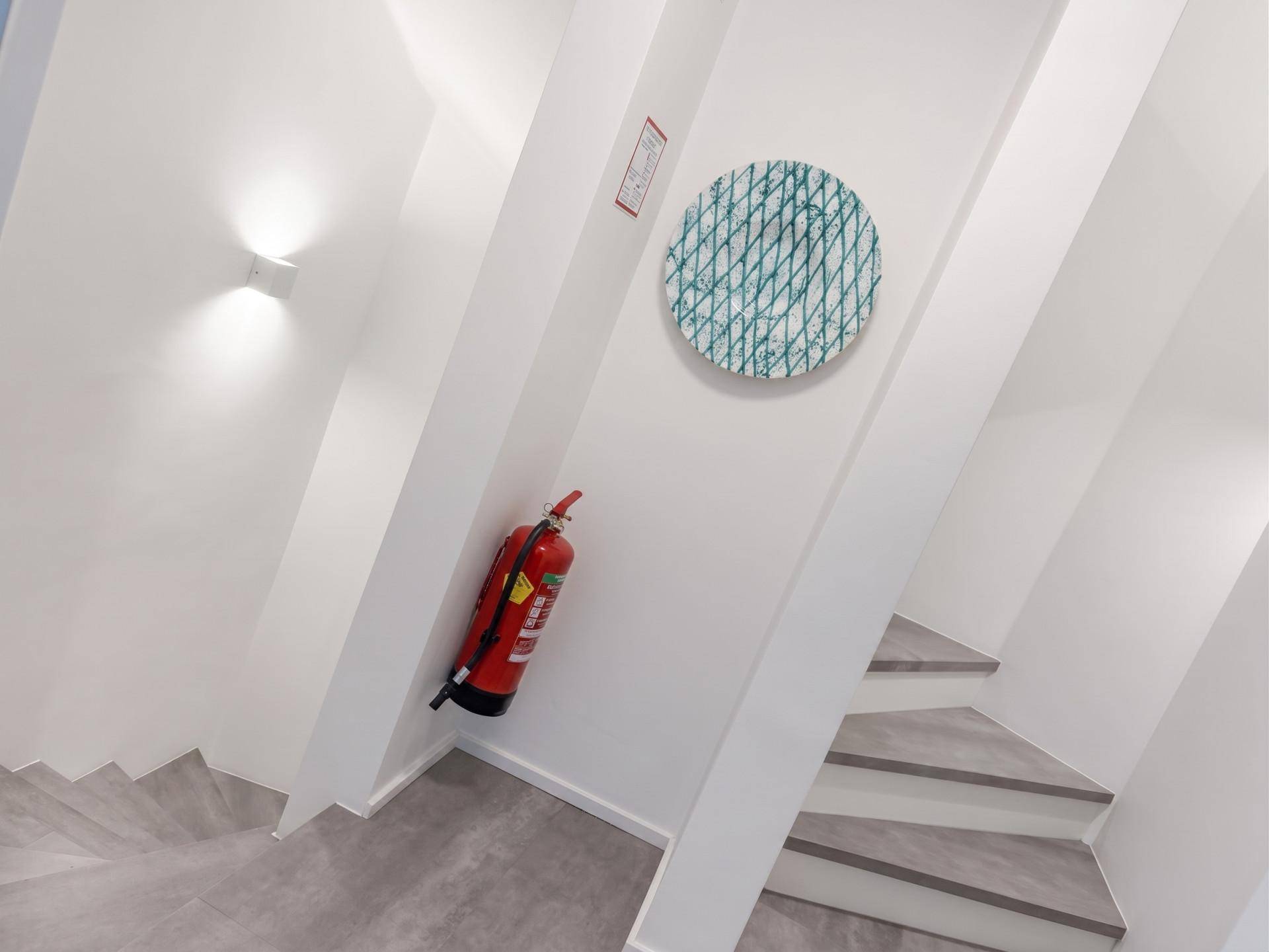 Modernes Treppenhaus mit grauen Stufen, weißen Wänden und einem sichtbaren Feuerlöscher.