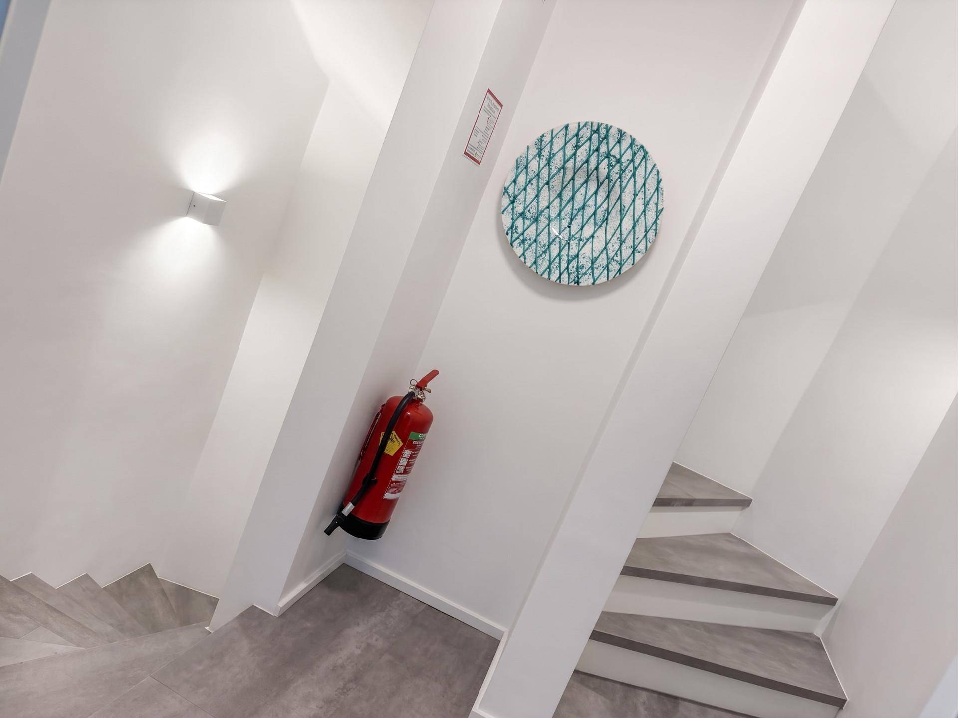 Modernes Treppenhaus mit grauen Stufen, weißen Wänden und einem Feuerlöscher an der Wand.