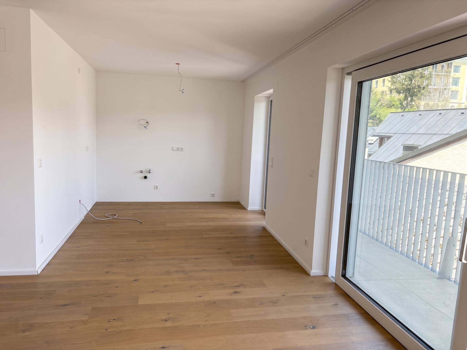 Heller, leerer Raum mit neuem Holzboden und Zugang zu einem Balkon, bereit zum Einrichten.