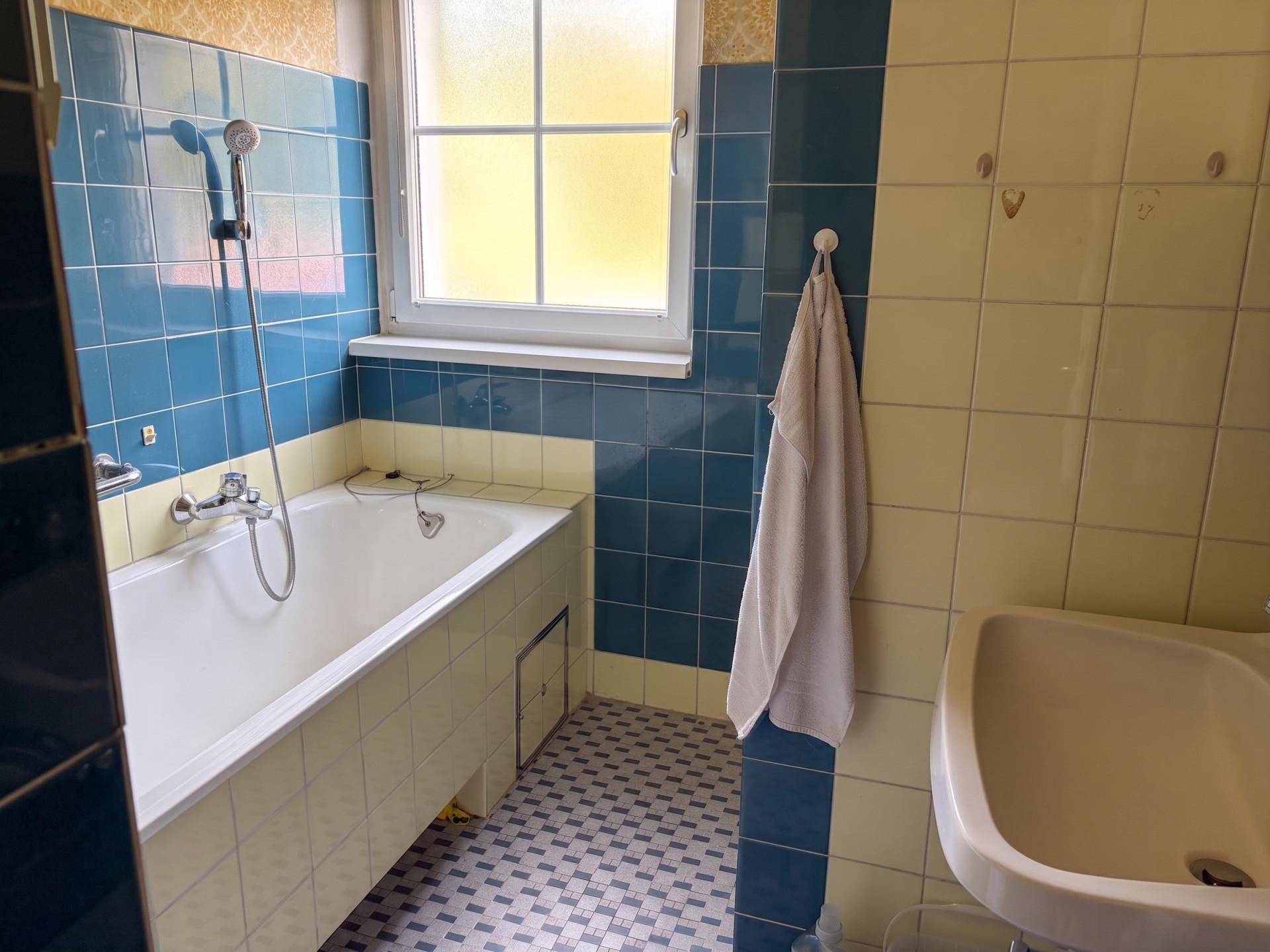 Badezimmer mit blauen und gelben Fliesen, Badewanne und Fenster.
