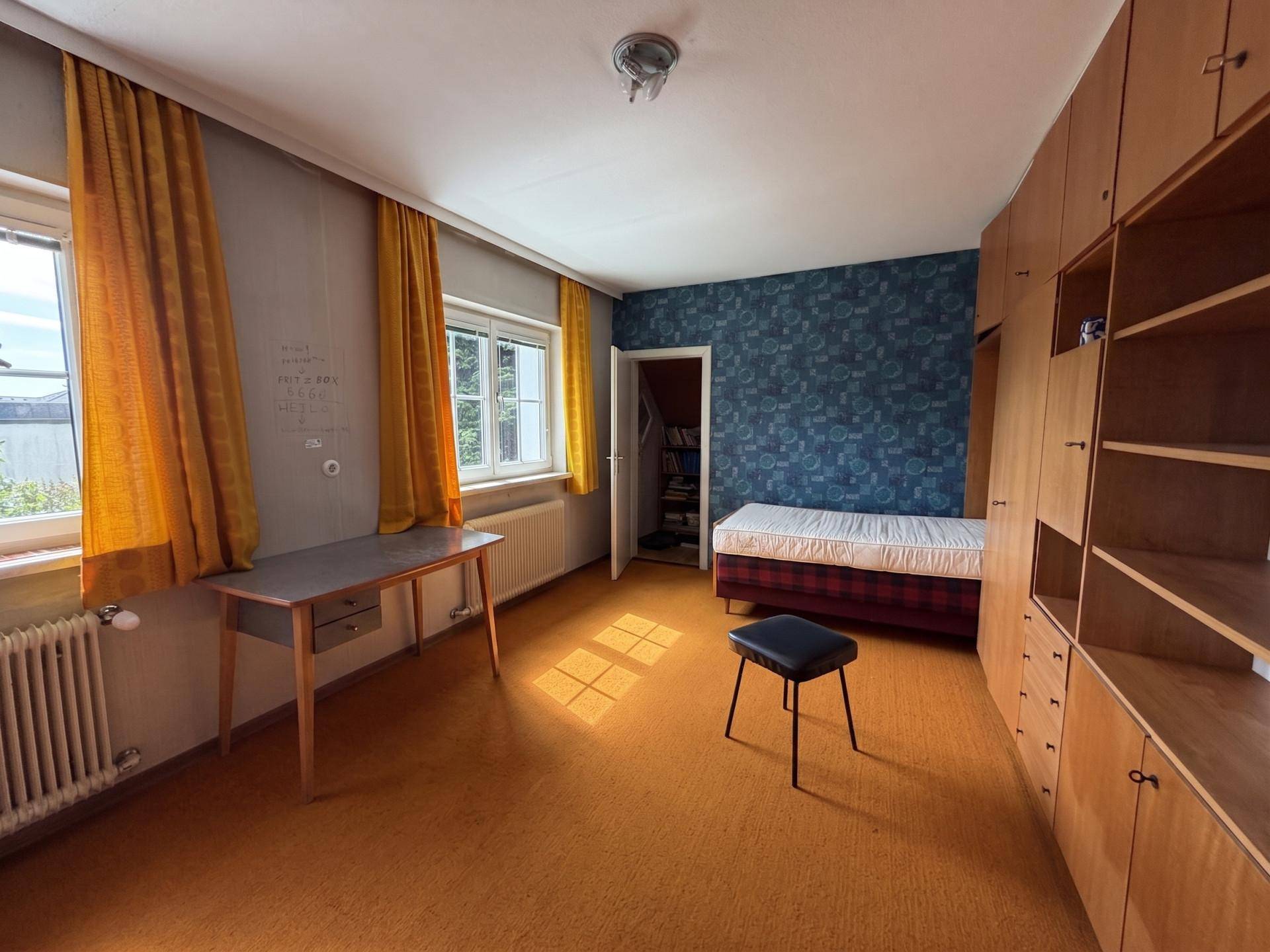 Schlafzimmer mit blauer Mustertapete, Holzschränken und orangefarbenen Vorhängen.