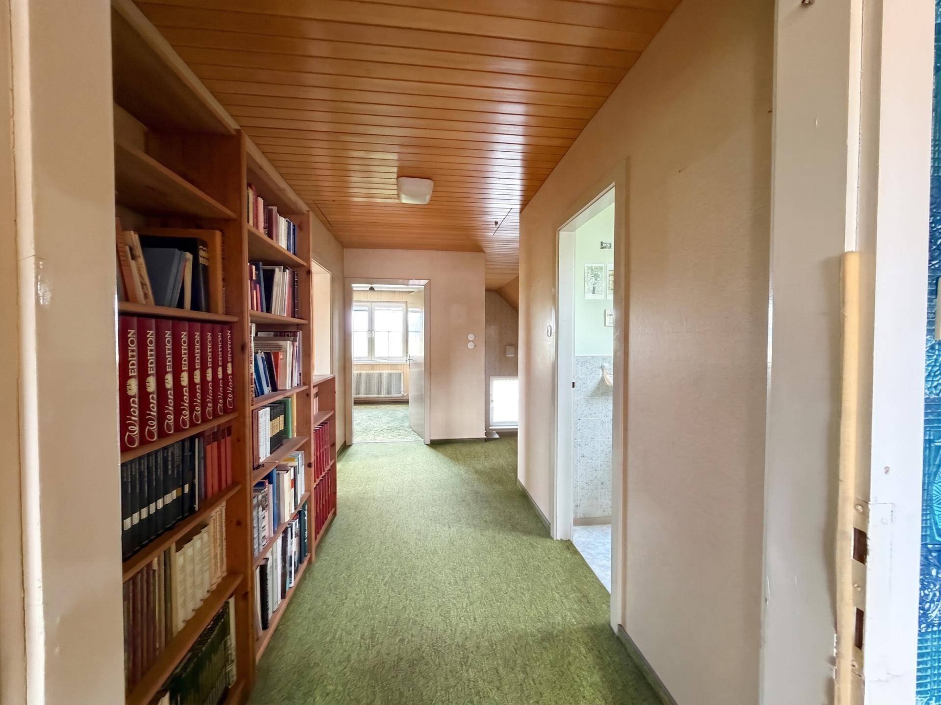 Langer Flur mit Teppichboden, Holzdecke und integriertem Bücherregal.