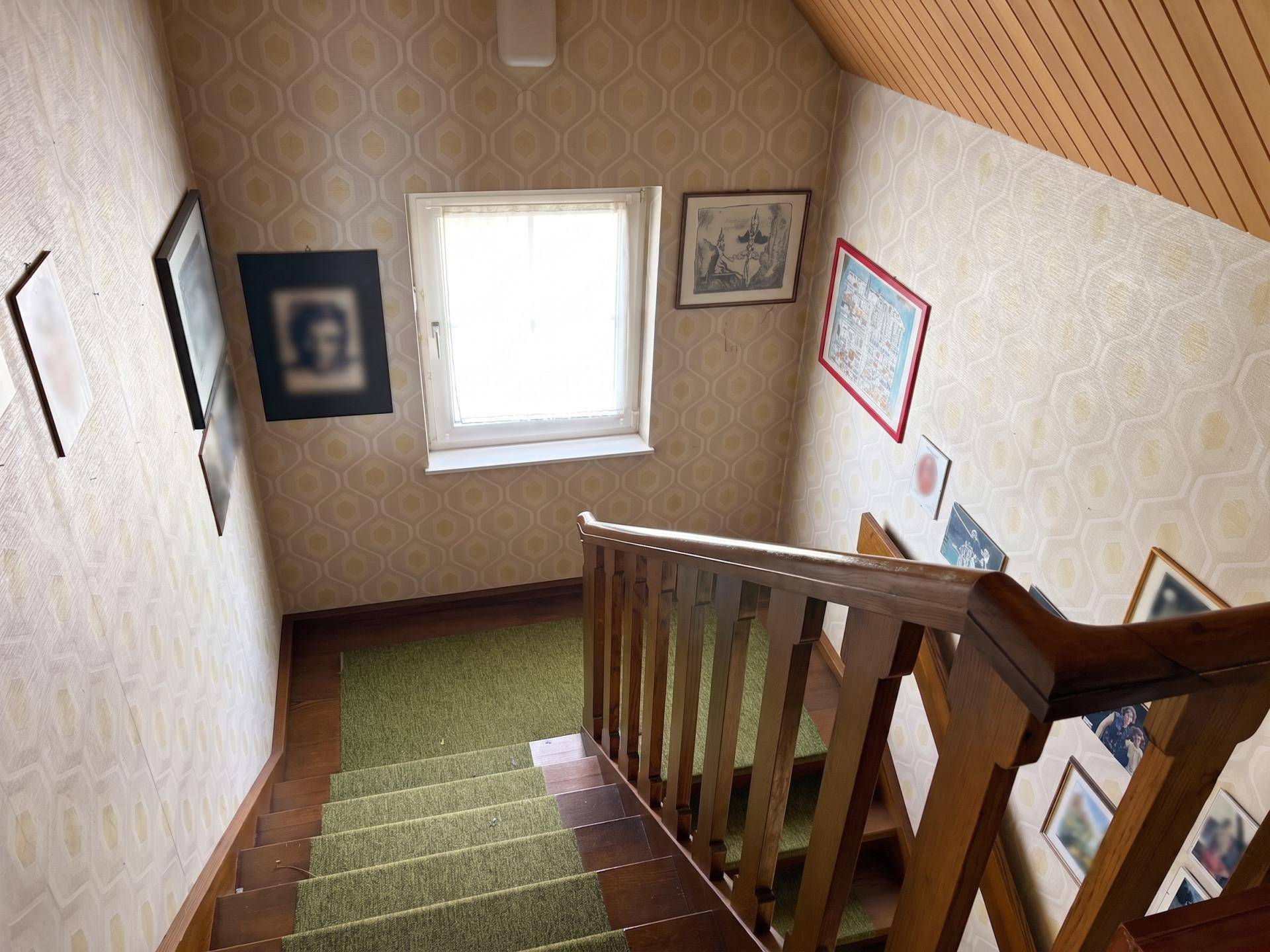 Treppenhaus mit Holzgeländer, Teppichstufen und gemusterter Tapete.