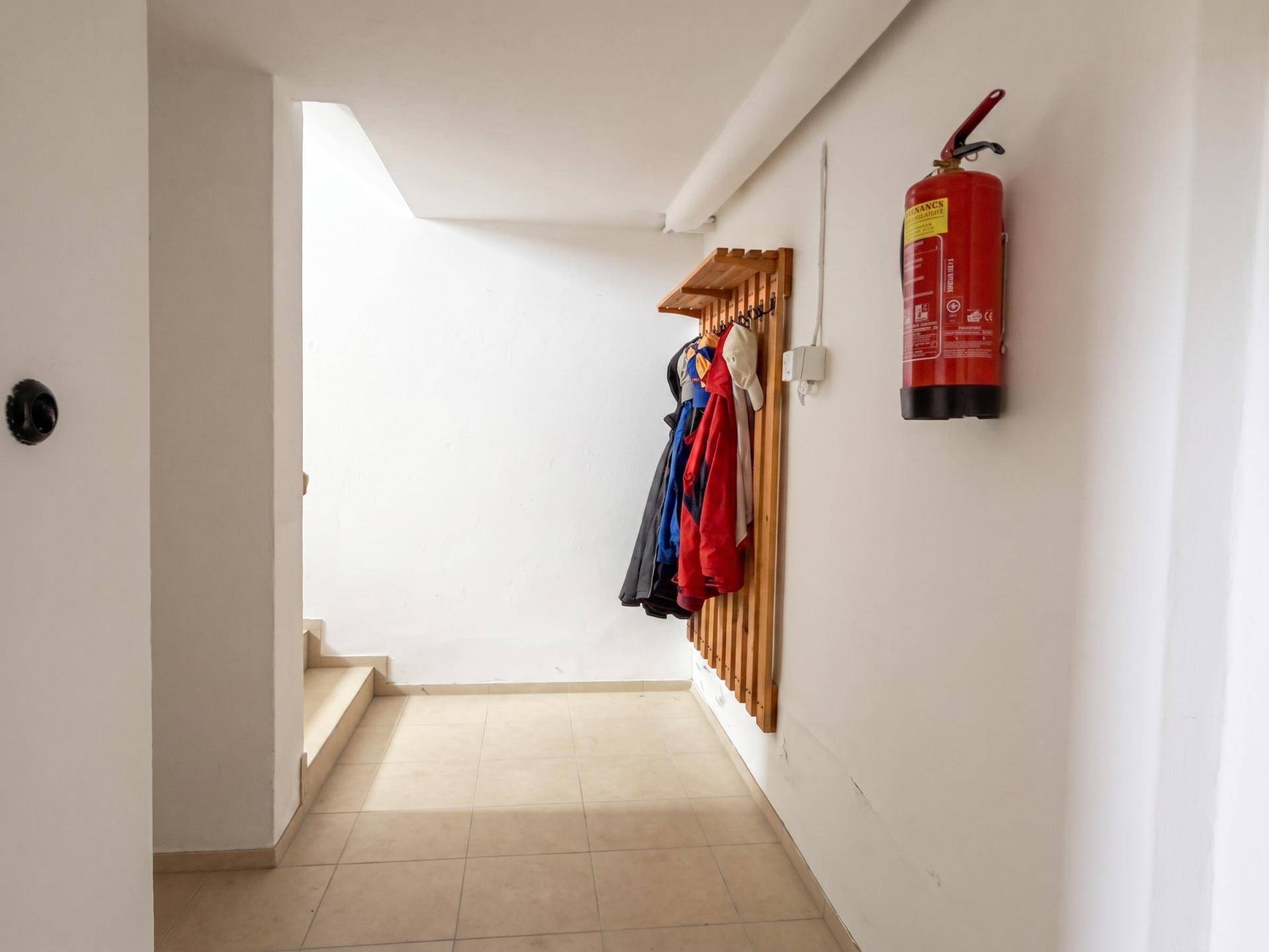 Heller Eingangsbereich mit Fliesenboden, Garderobe und Feuerlöscher.