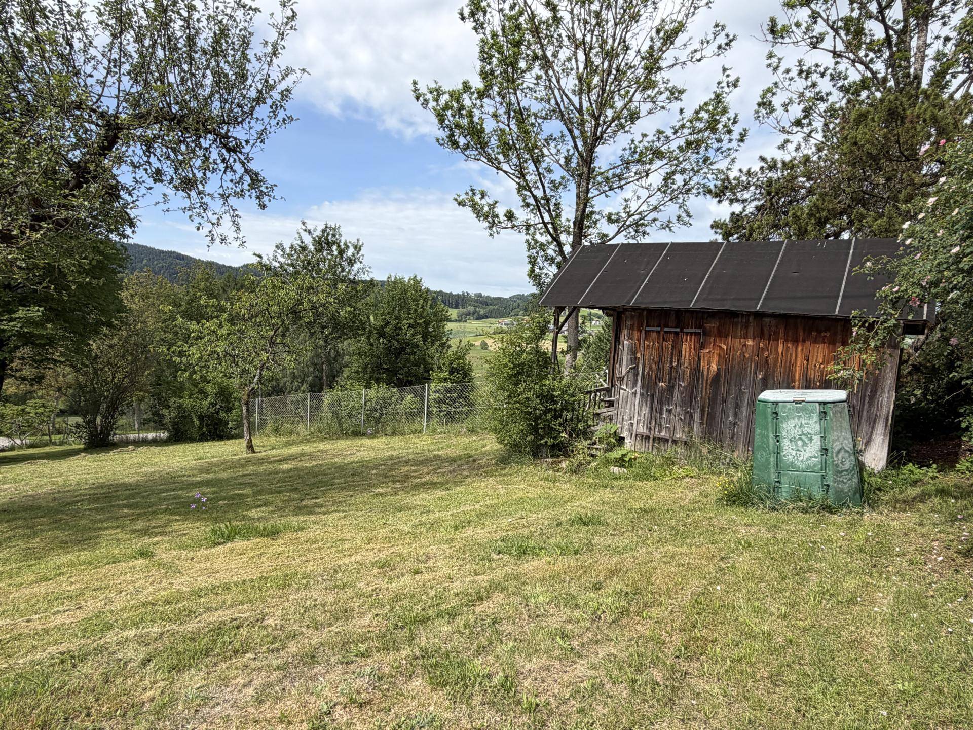 Gepflegter Gartenbereich mit Holzschuppen, Komposter und weitem Blick in die Natur.