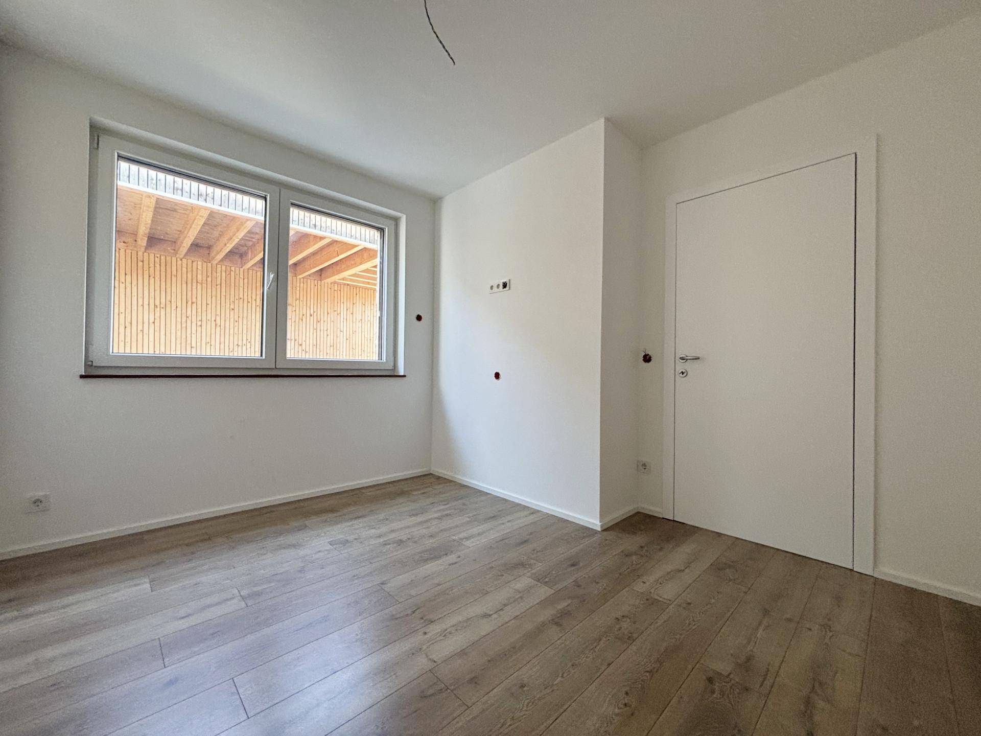 Helles Schlafzimmer mit Laminatboden, weiß gestrichenen Wänden und Blick auf den Carport.