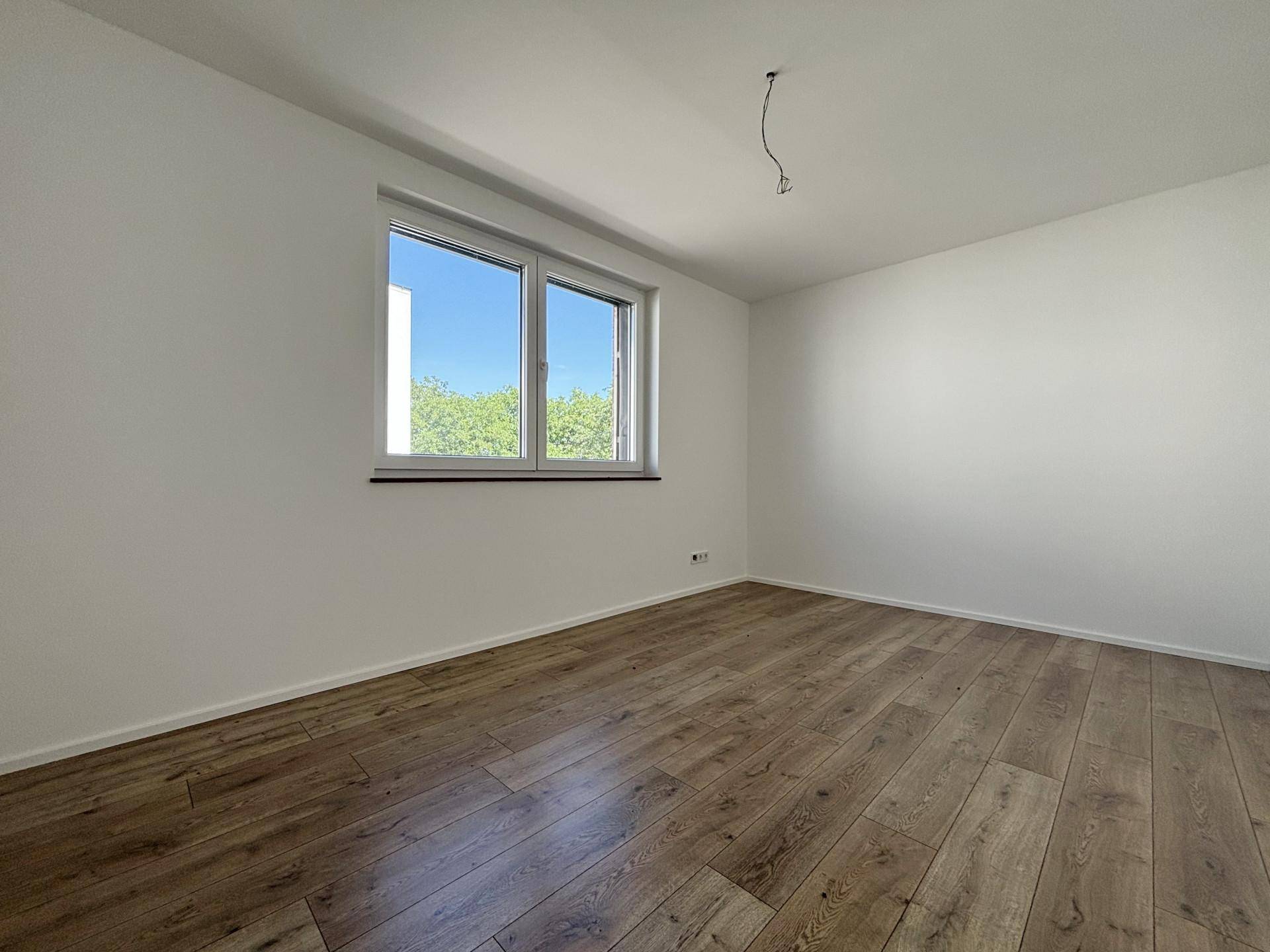 Helles Schlafzimmer mit Laminatboden, weißen Wänden und angenehmem Blick ins Grüne.