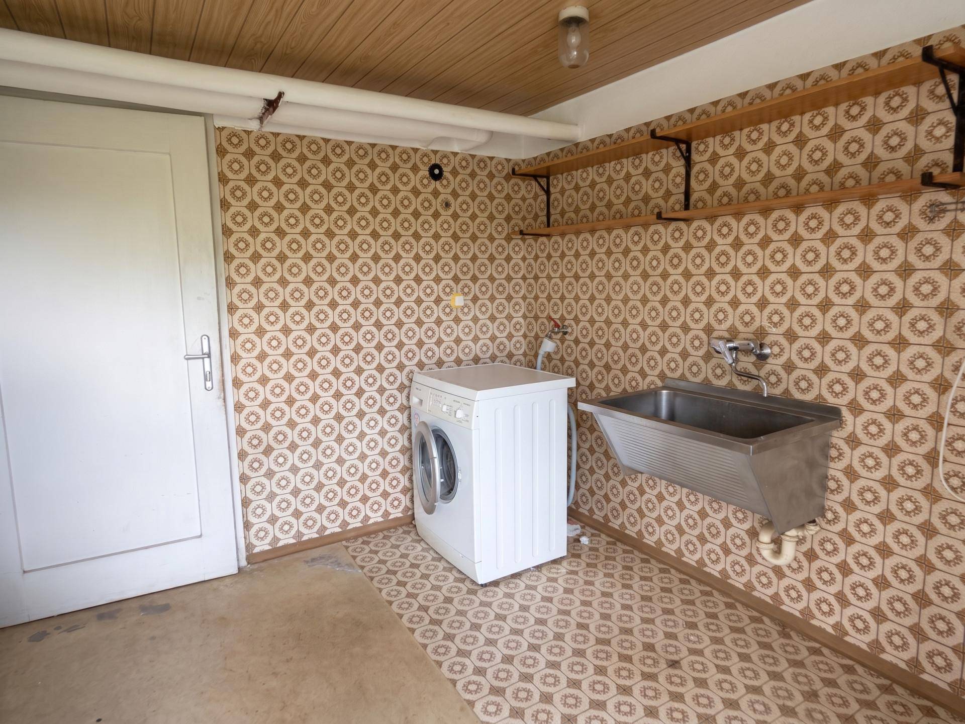 Waschküche im Keller mit Waschmaschine, Waschbecken und gemusterter Tapete.