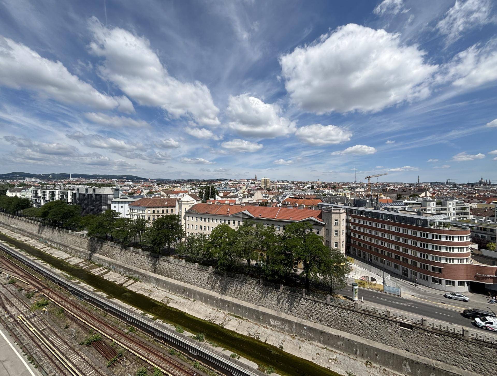 Weitläufiger Blick über die Stadt mit Gebäuden, Bahngleisen und bewölktem Himmel.