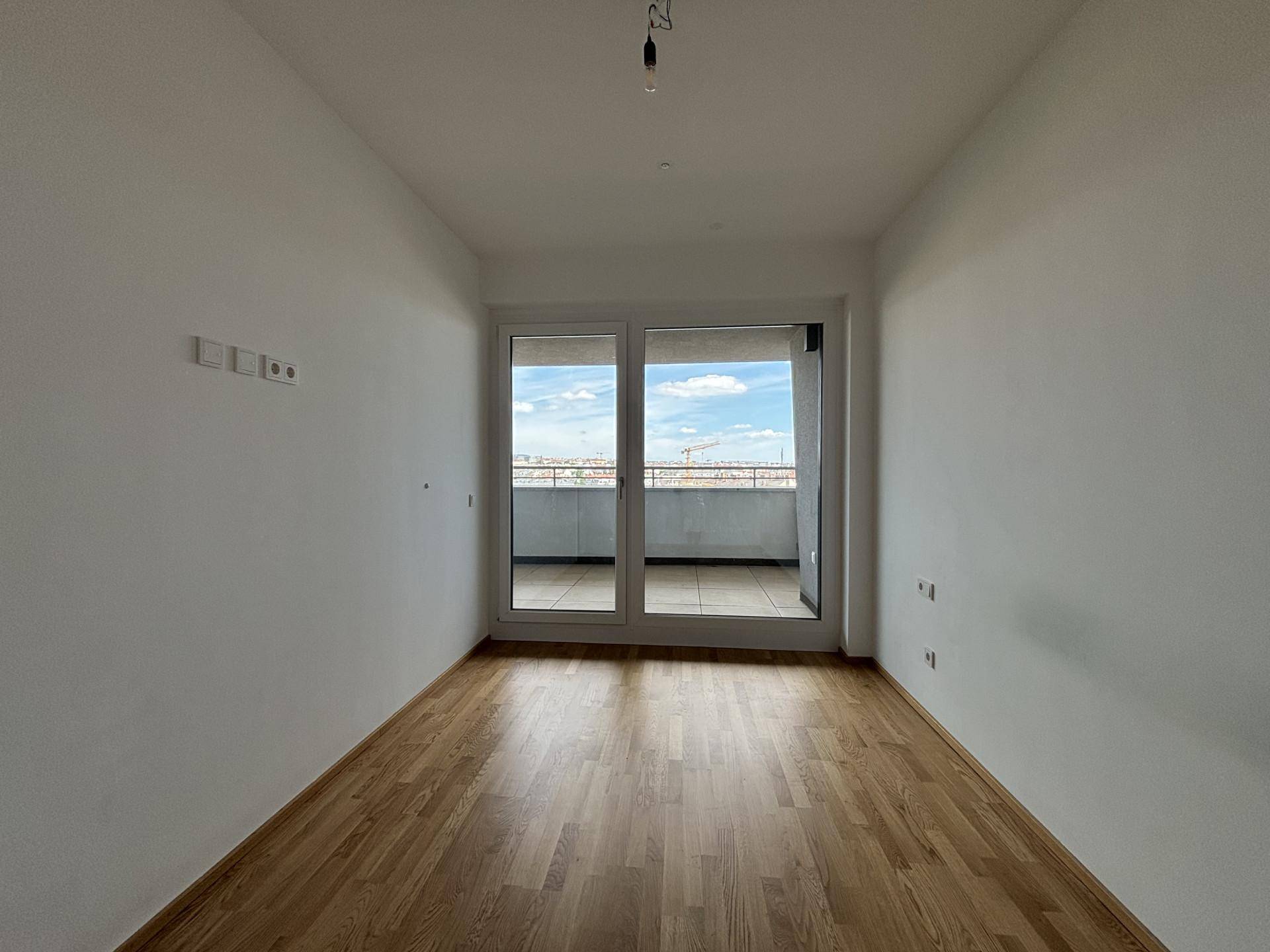 Heller, leerer Raum mit Holzboden und Balkonzugang, ideal für verschiedene Nutzungen.