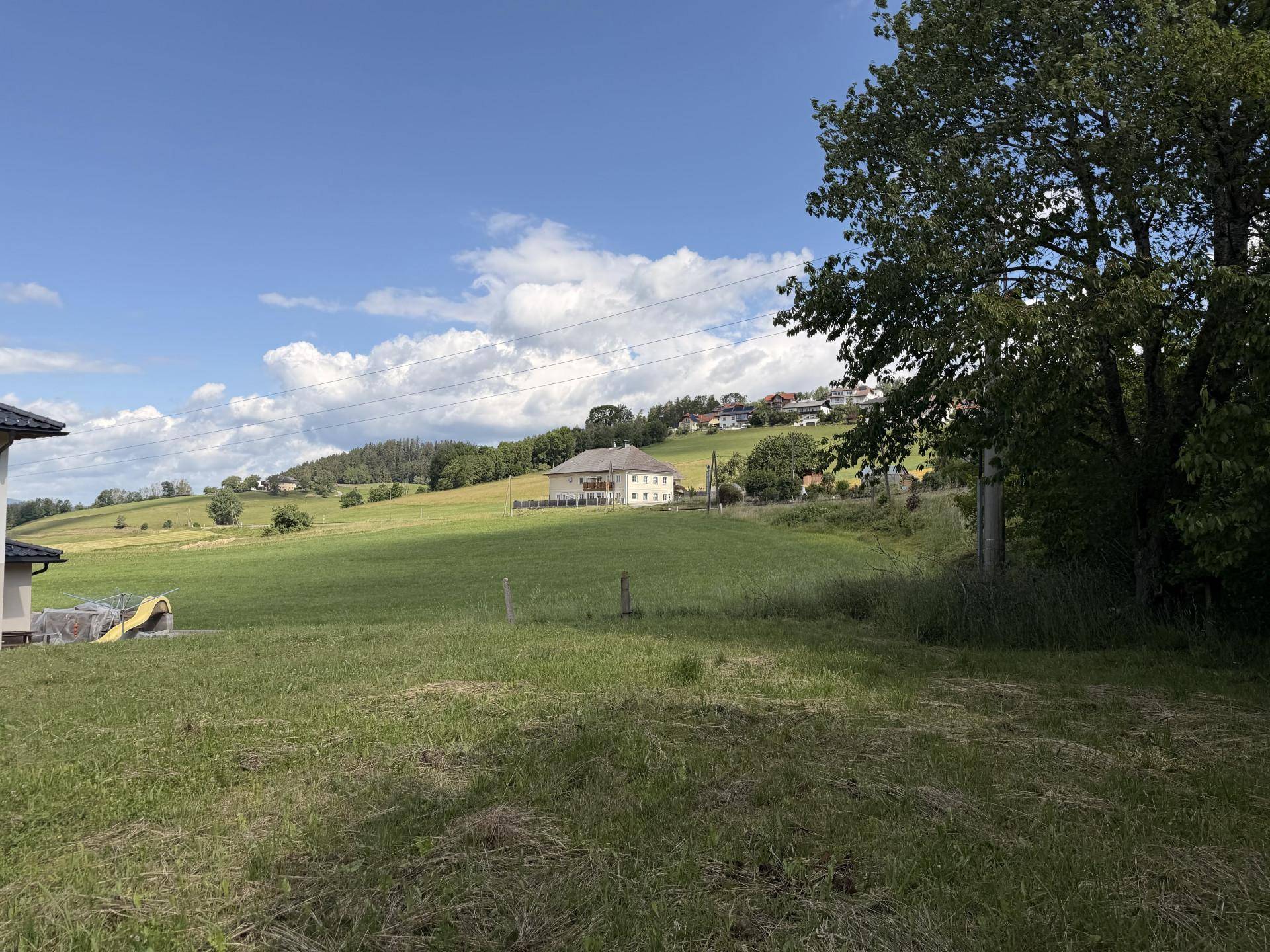 Malerische Hügellandschaft mit grünen Wiesen, einem großen Haus und weiteren Gebäuden am Horizont.