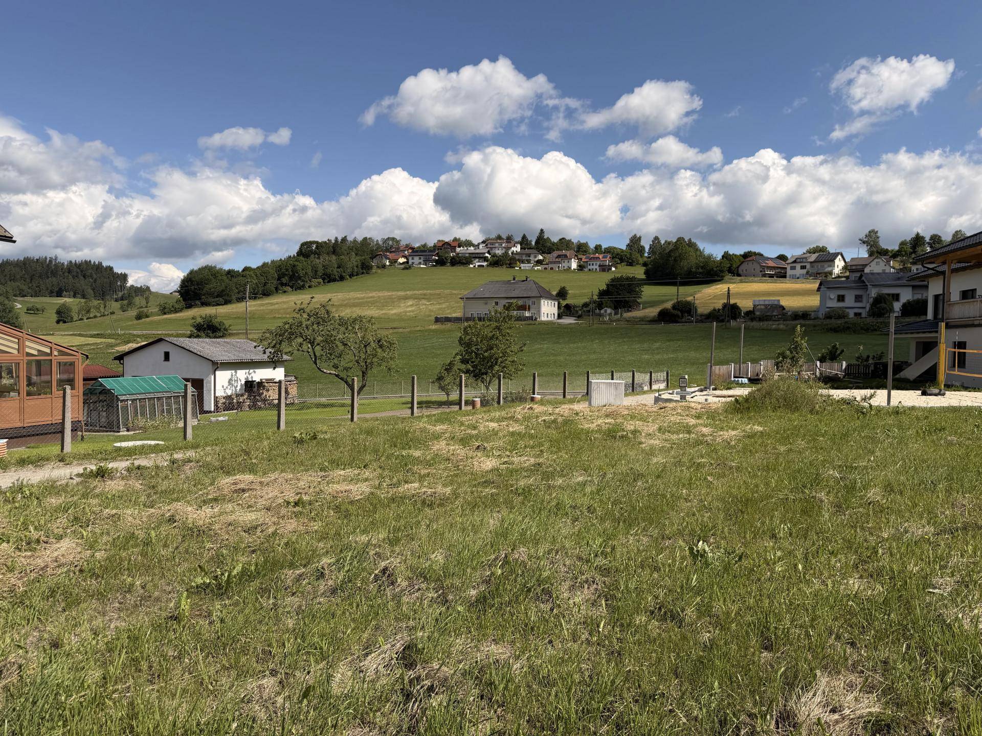 Panoramablick über eine hügelige Landschaft mit einem Dorf und vorbereiteten Flächen im Vordergrund.