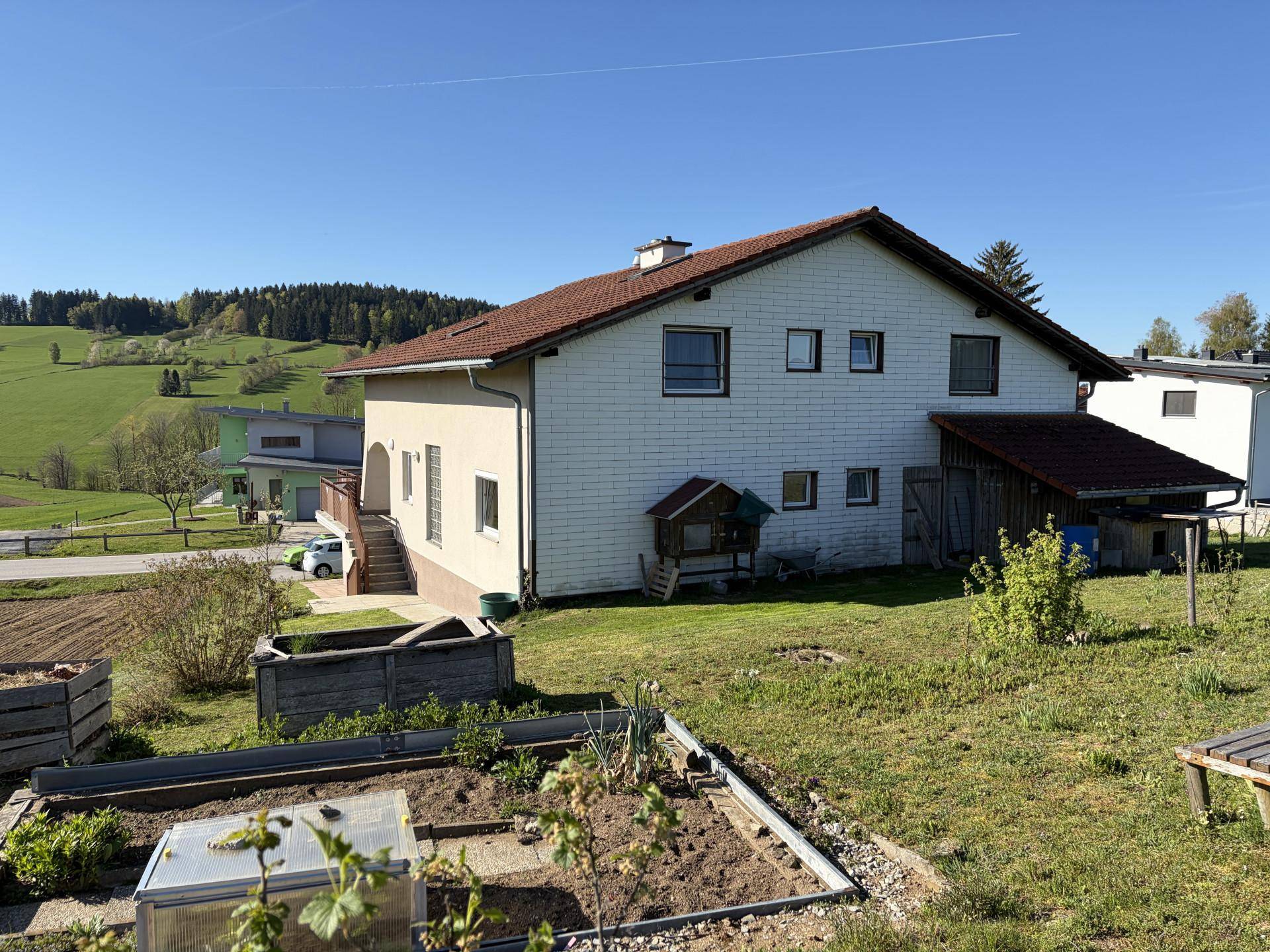 Rückansicht des Hauses mit Gartenbereich, Hochbeeten und Blick auf die grüne Landschaft.
