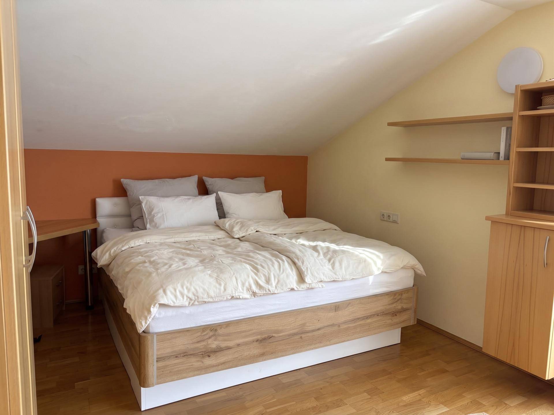 Schlafzimmer im Dachgeschoss mit Holzbett, schrägen Wänden und einfacher Einrichtung.