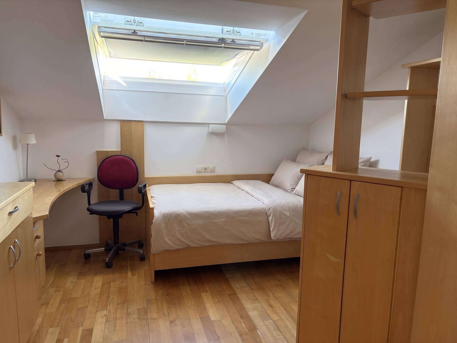 Schlafzimmer mit Schreibtisch, Holzboden und Dachfenster, das viel Tageslicht hereinlässt.