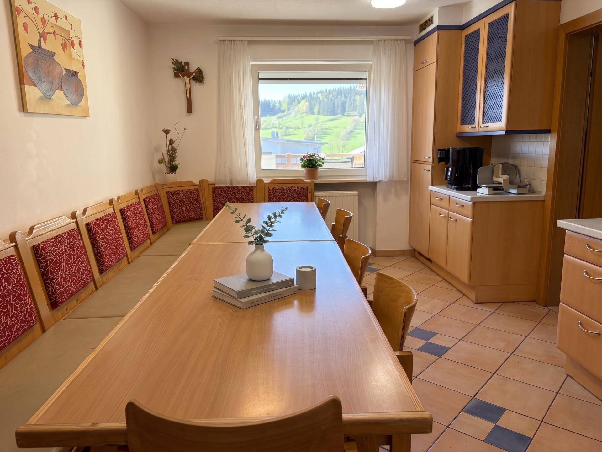 Traditionelle Küche mit großem Esstisch, Holzbänken und Blick ins Grüne.