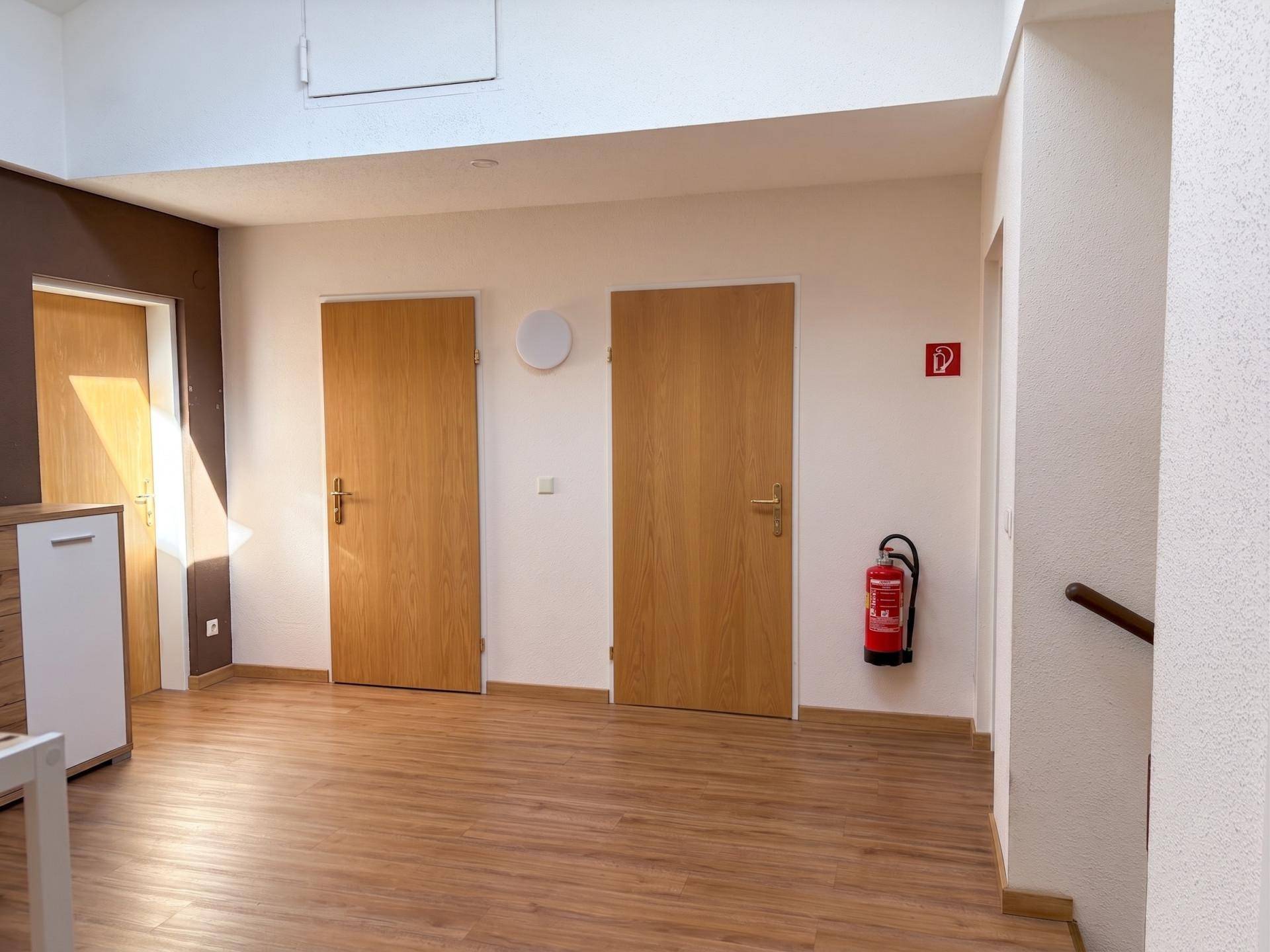 Heller Flur mit Holzboden und mehreren Türen, ausgestattet mit einem Feuerlöscher.