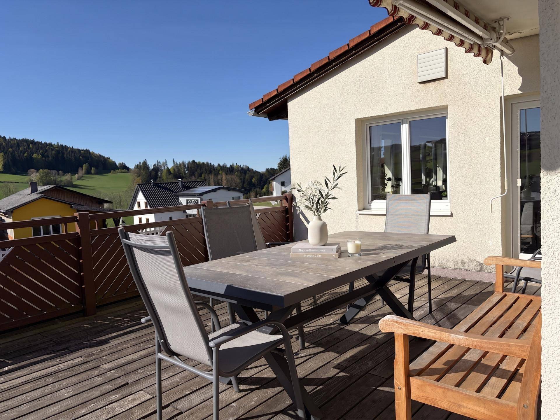 Helle Terrasse mit Holzboden und Gartenmöbeln, angrenzend an das Haus mit Blick ins Grüne.