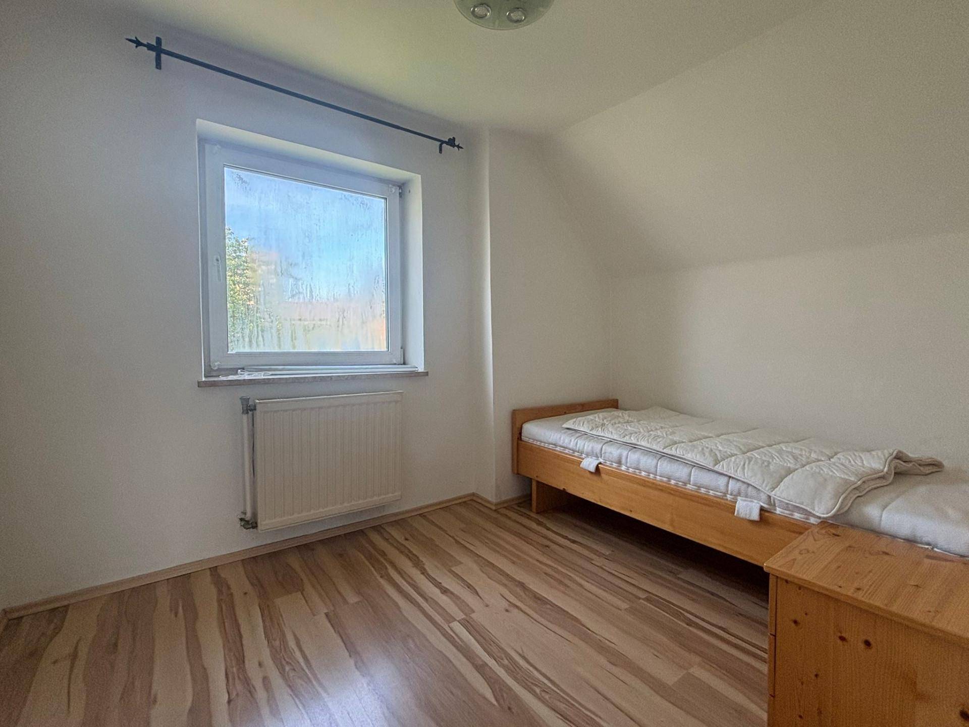 Gemütliches Schlafzimmer mit Einzelbett, Holzmöbeln und Laminatboden, gut beleuchtet.