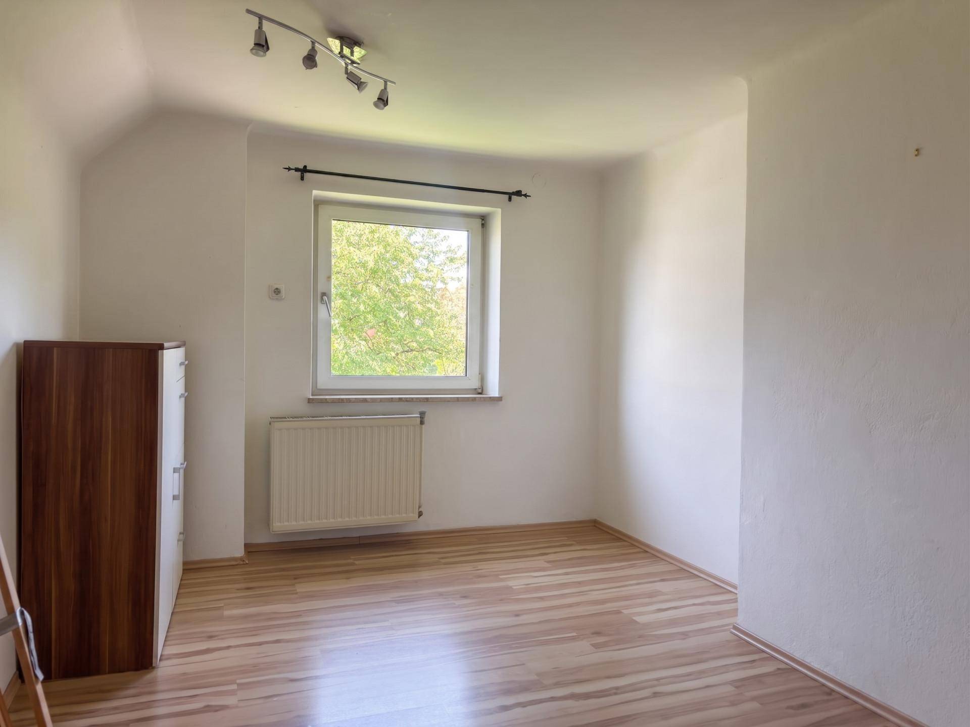 Helles Zimmer mit Laminatboden, weiß gestrichenen Wänden und einem Fenster mit Ausblick.