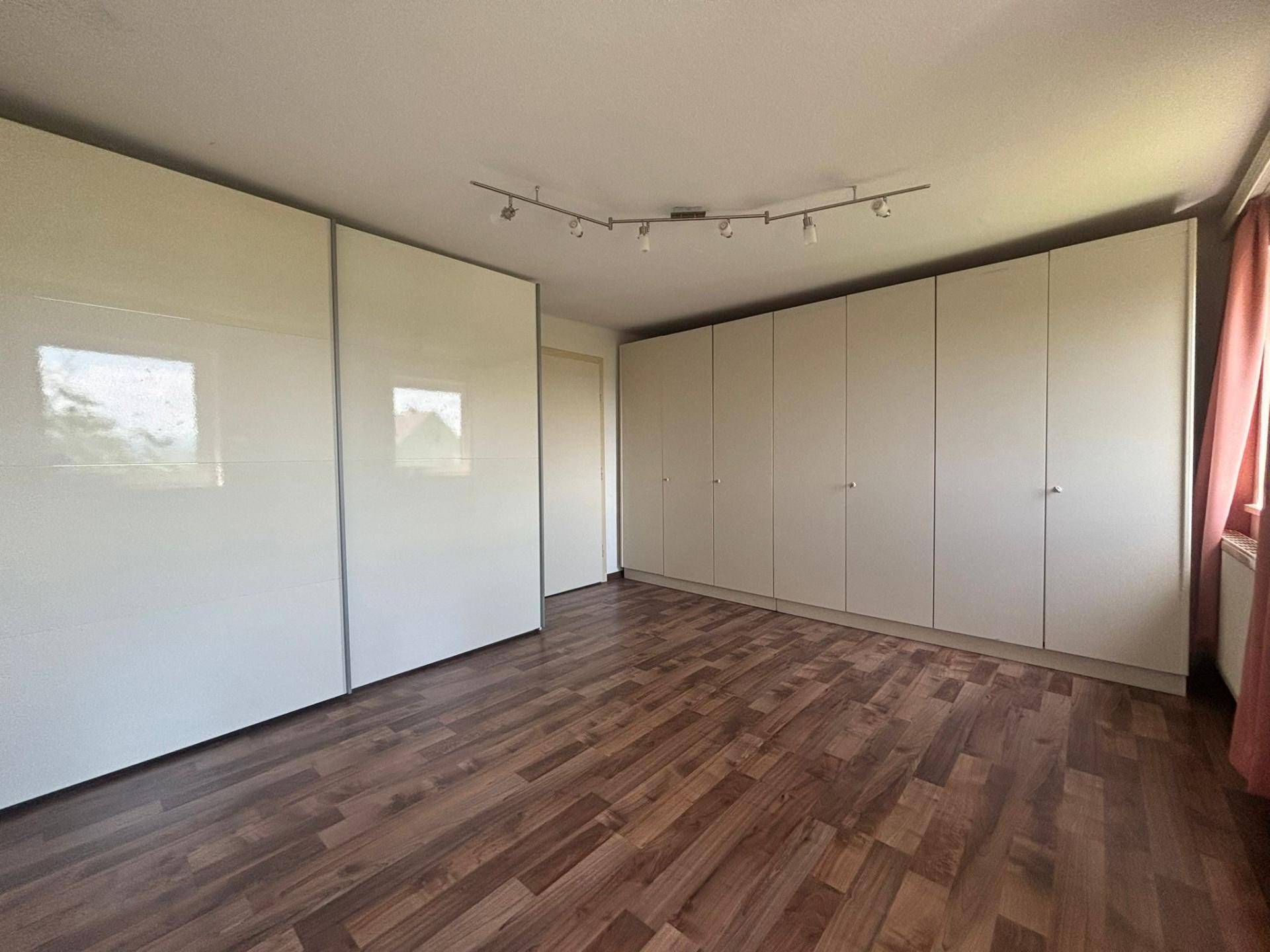 Geräumiges Schlafzimmer mit großen, glänzenden Einbauschränken und Laminatboden.