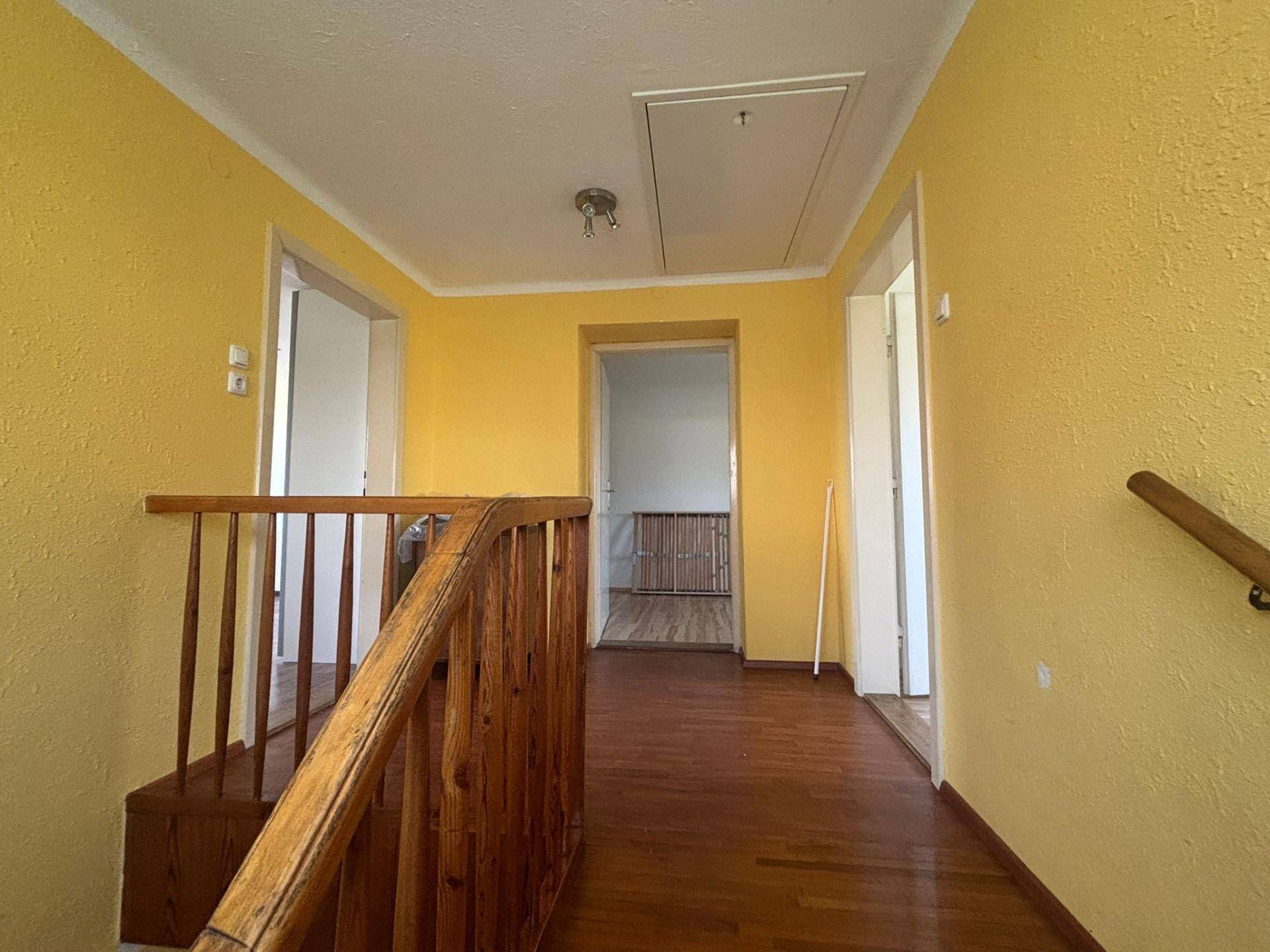 Heller Flur mit gelben Wänden, Holzgeländer und Laminatboden, führt zu weiteren Räumen.