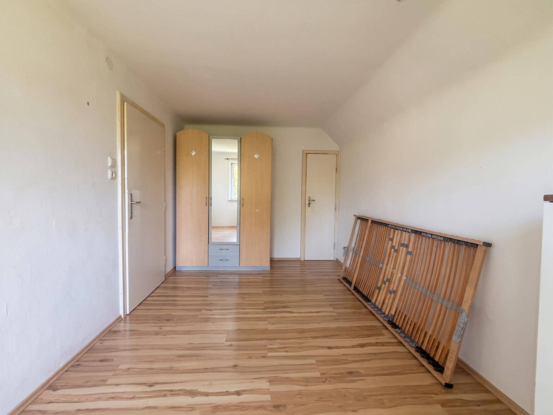 Geräumiges Schlafzimmer mit Laminatboden, Kleiderschrank und einem Lattenrost.