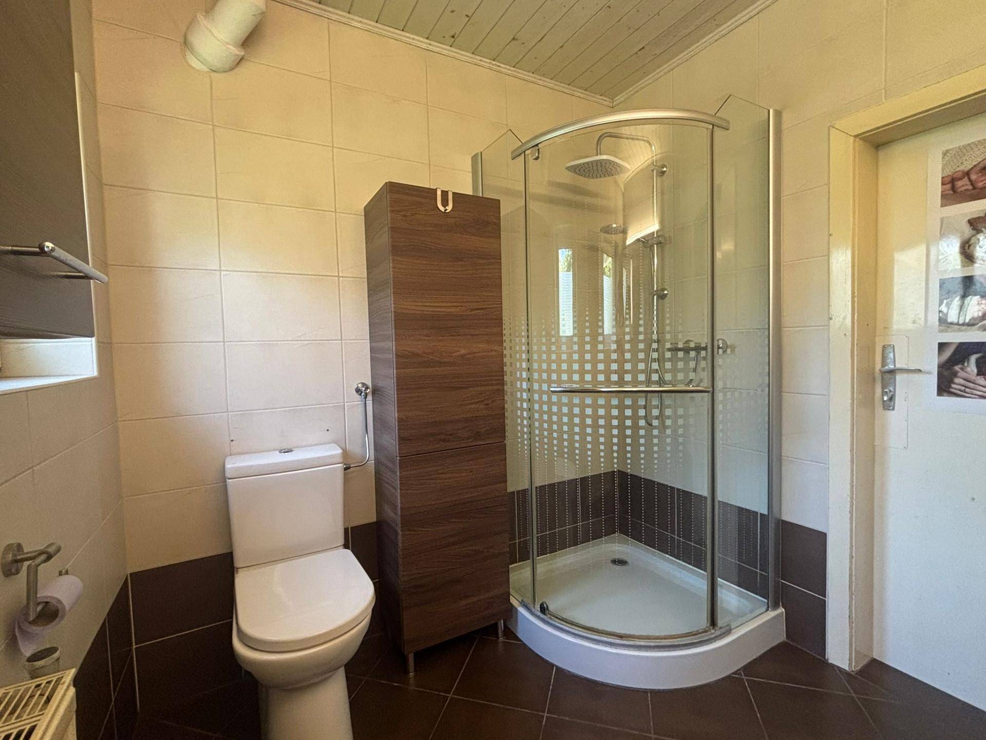 Badezimmer mit Duschkabine, WC und braun-beigen Fliesen, funktional eingerichtet.