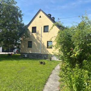 Gelbes Einfamilienhaus mit Satteldach und grünem Garten unter blauem Himmel.