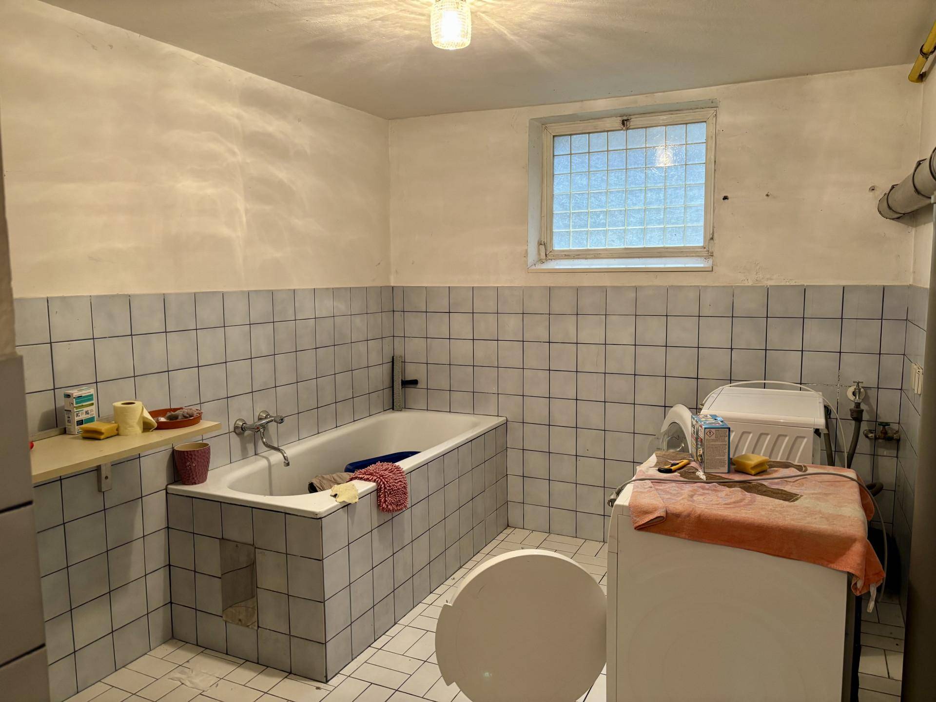 Einfaches Badezimmer im Keller mit Badewanne, Waschmaschine und Fliesen.