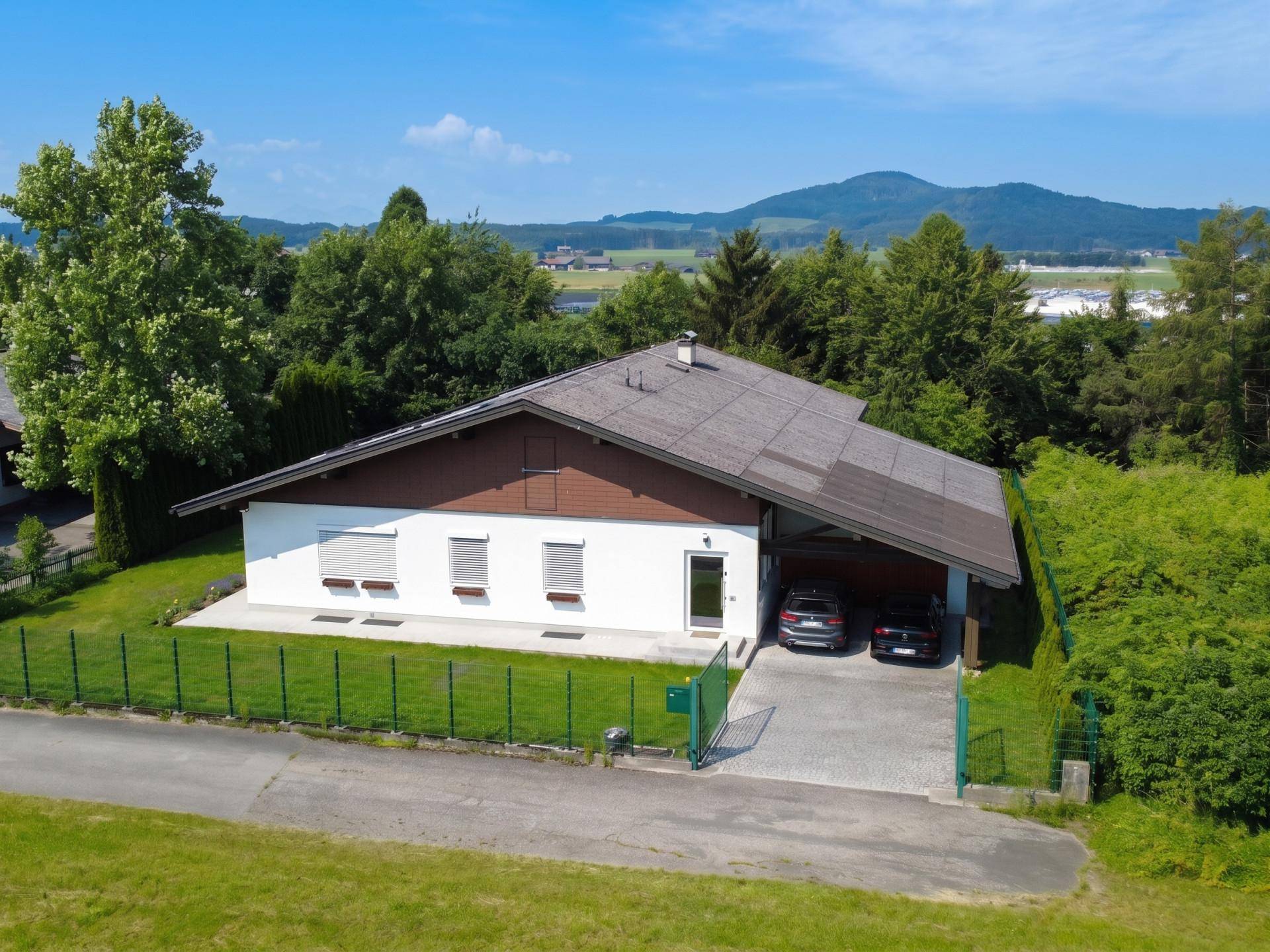 Einfamilienhaus mit Carport und Photovoltaikanlage, umgeben von viel Grün.